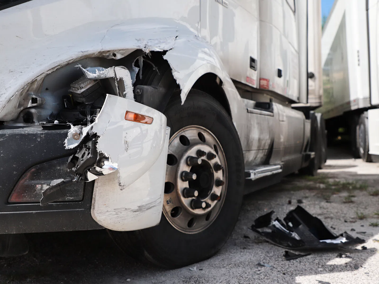 Close-up of a white truck with significant front damage and debris on the ground next to the tire.