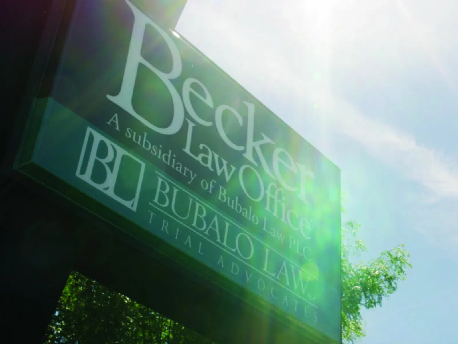 Becker Law Office sign with sun flare and blue sky background in an outdoor setting