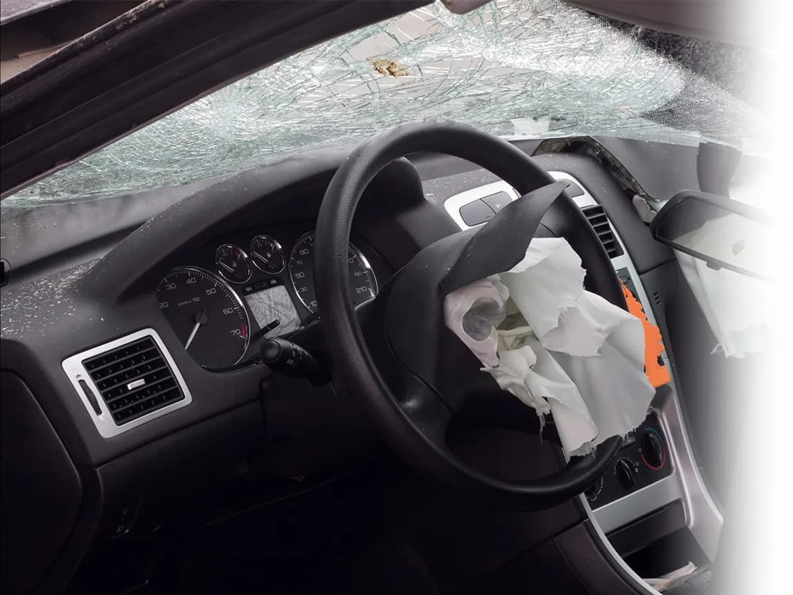 Car interior showing deployed airbags and shattered windshield after a crash impact.