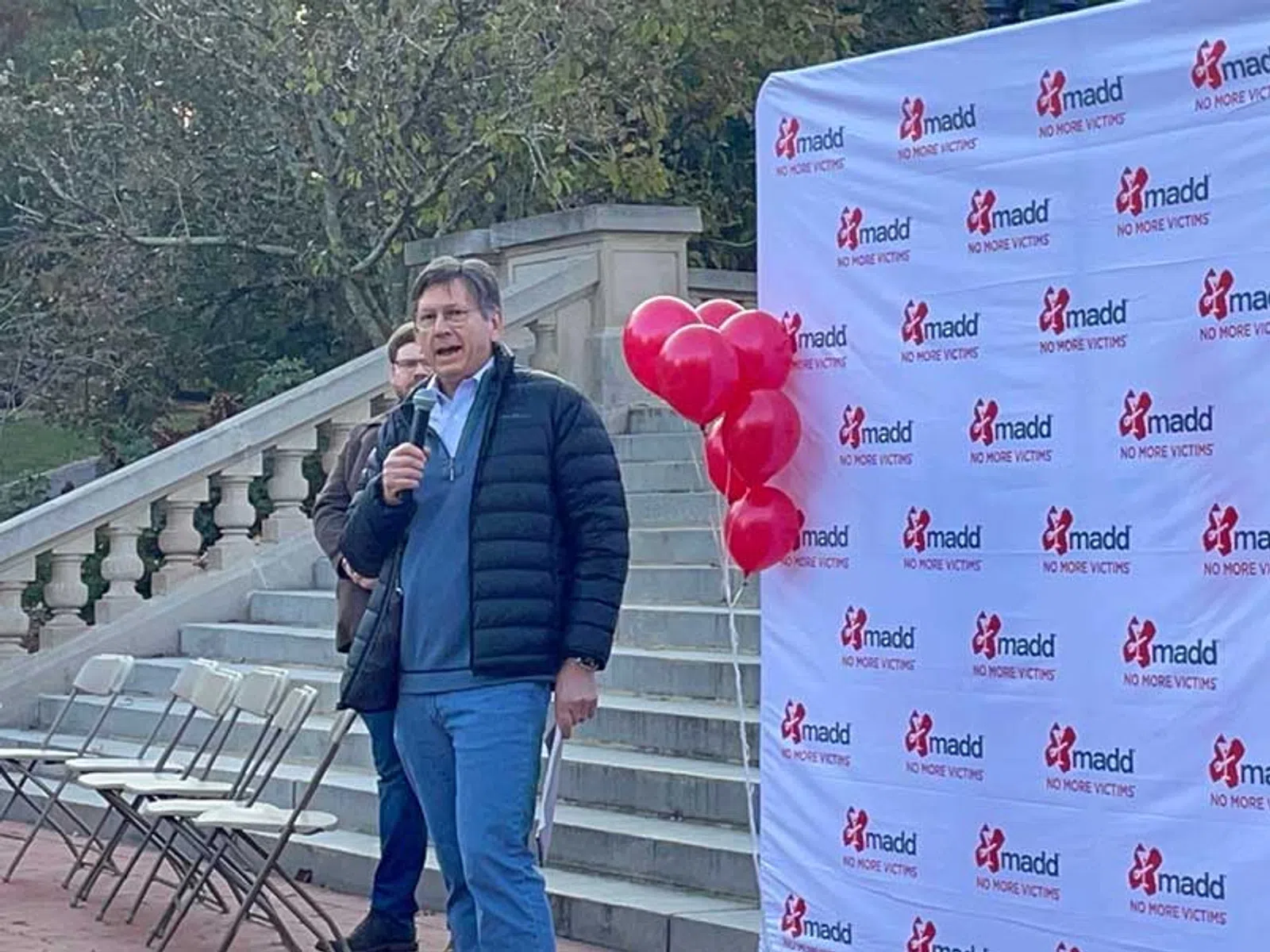 Man speaking at outdoor event with MADD banner and red balloons promoting no more victims campaign