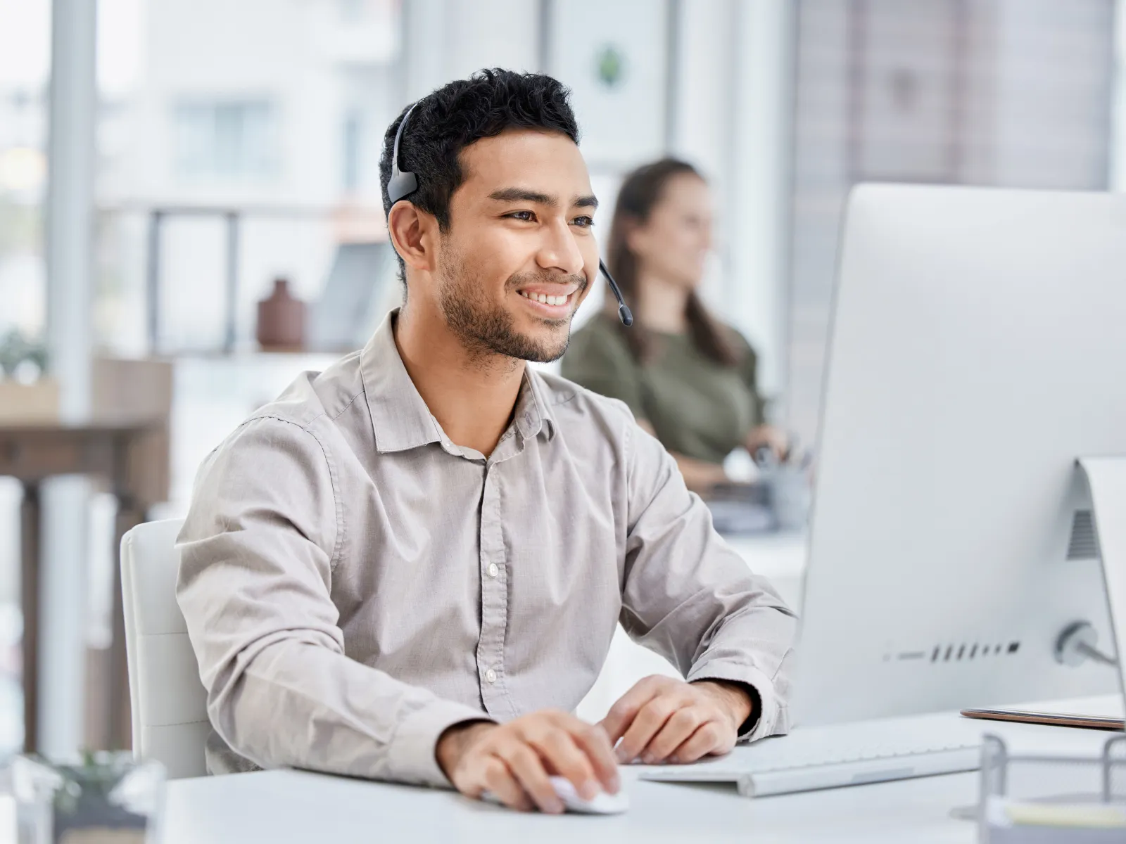 Smiling customer service representative using a computer in a modern office setting.