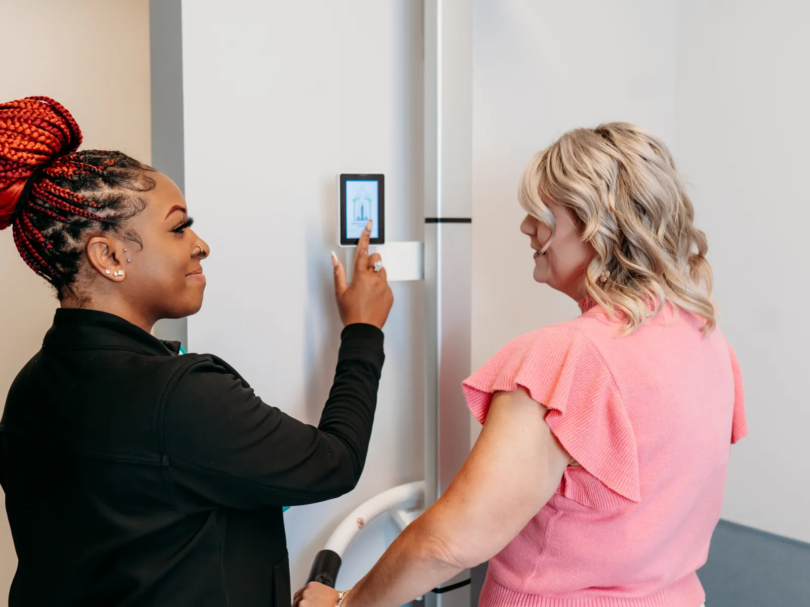 Two women interacting with a digital touchscreen panel on a modern refrigerator in a kitchen setting