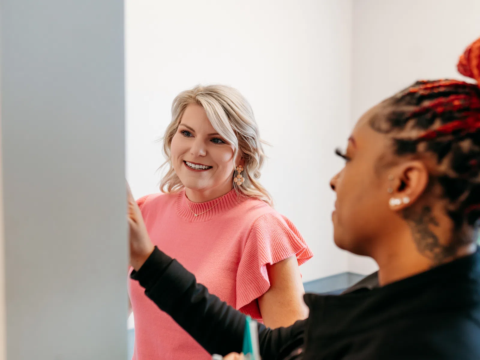 Two women collaborating in an office, one pointing at a screen and the other attentively smiling and listening.