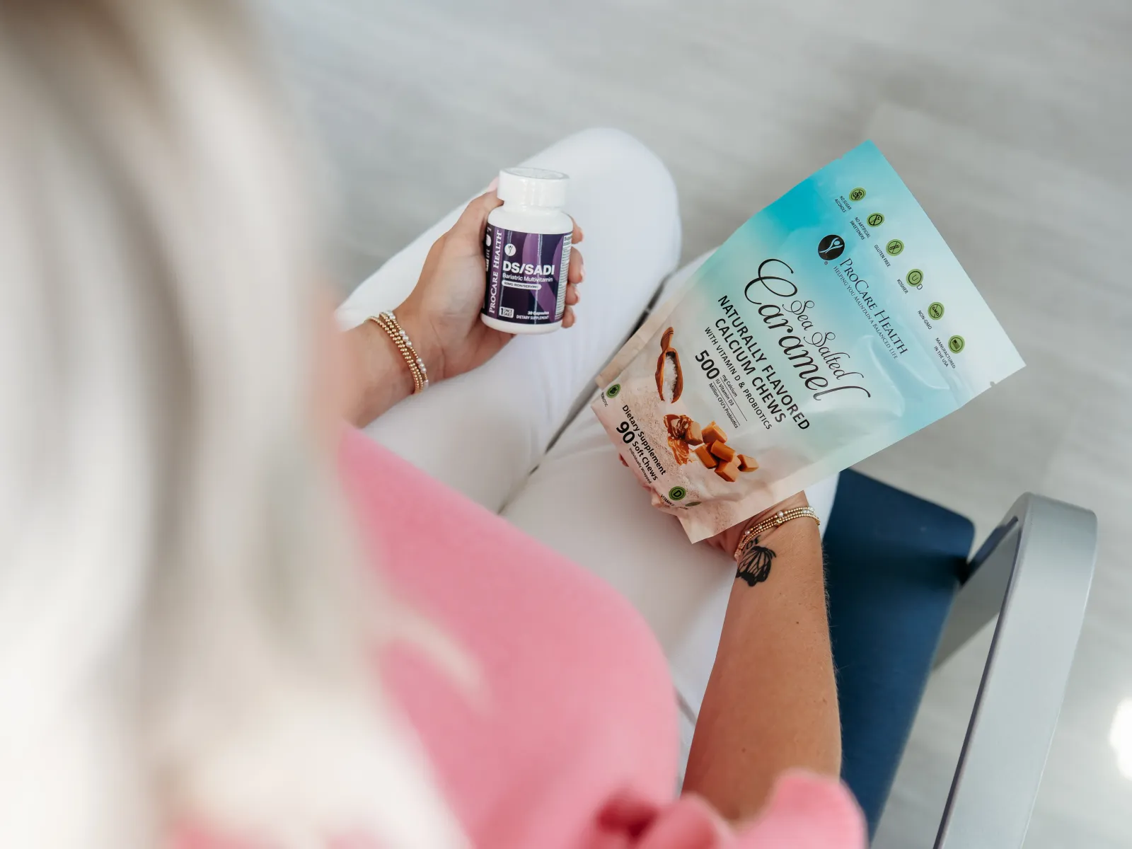Person holding a bottle of supplements and a bag of naturally flavored caramel collagen chews, seated indoors.