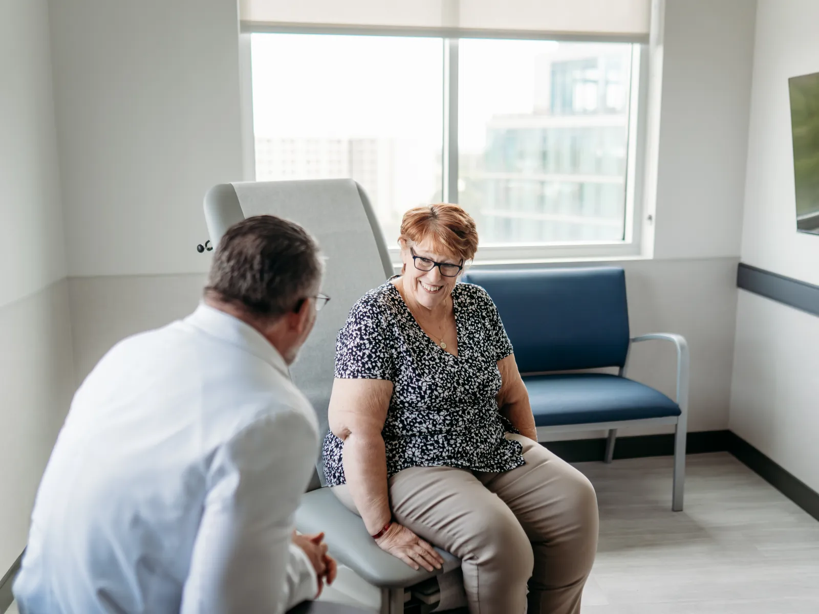 Senior woman smiling and talking with male doctor in a bright medical office during consultation.