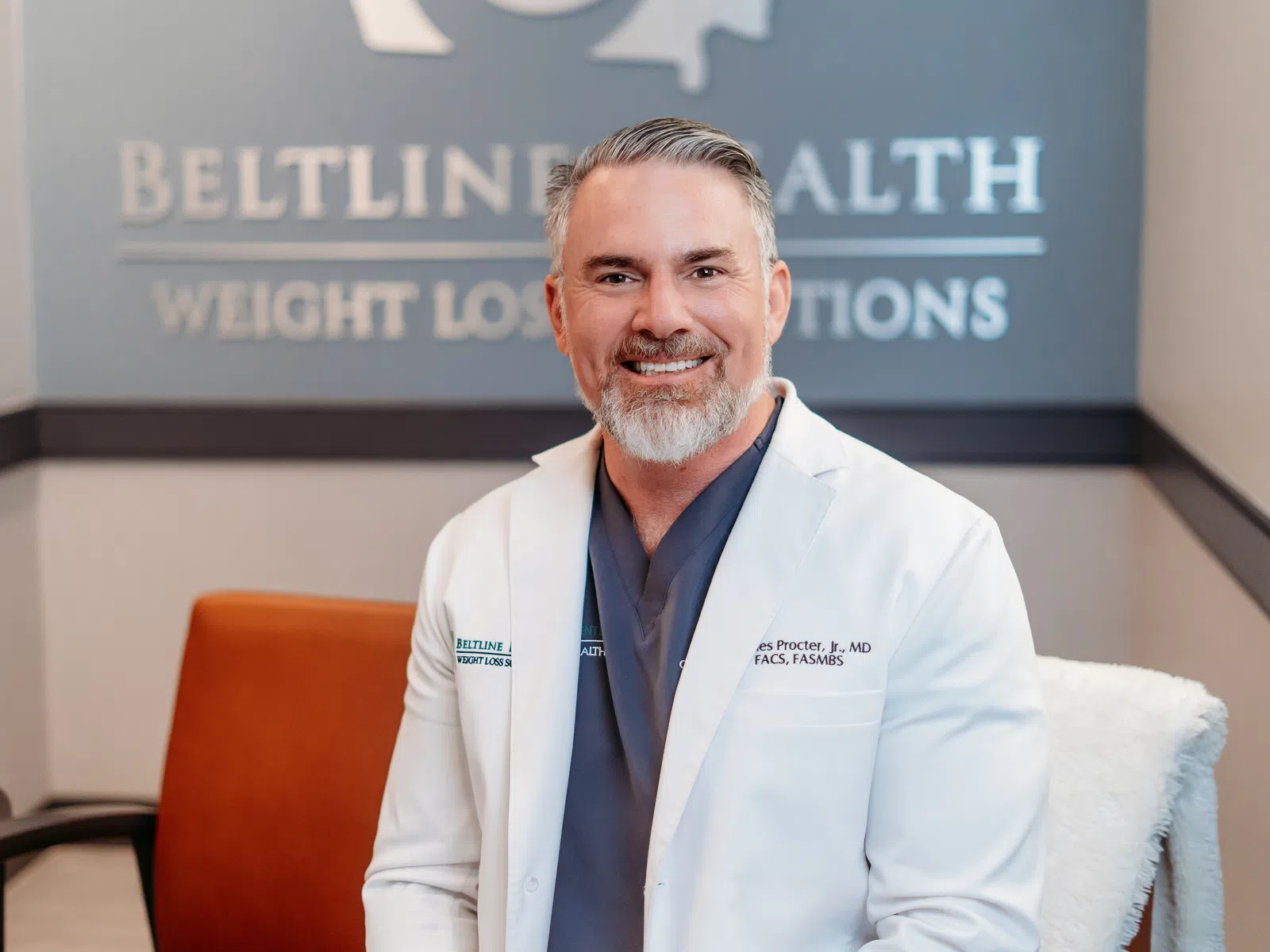 Smiling male doctor in white coat sitting in clinic with Beltline Health weight loss sign behind him