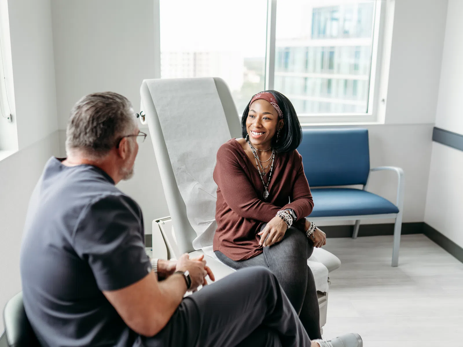 Smiling woman talking with male doctor in modern medical office with natural light and city view windows