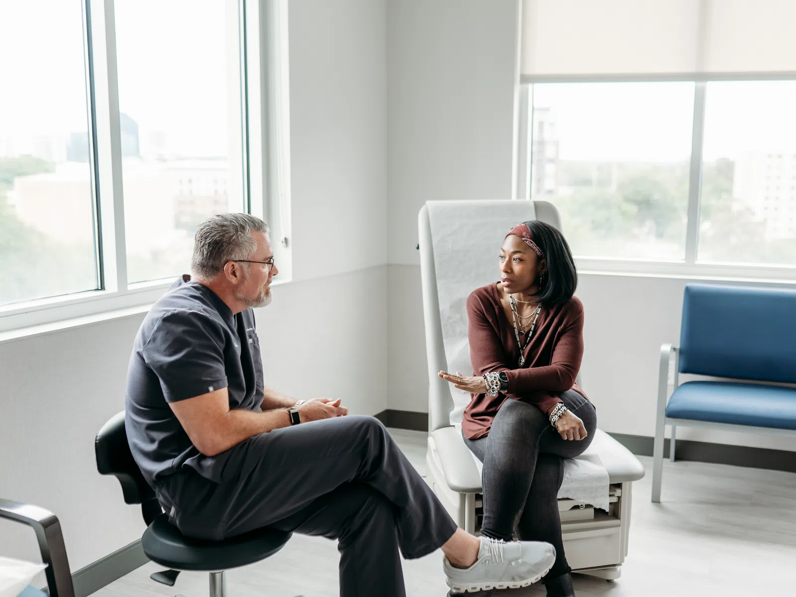 Female patient discussing health concerns with doctor in bright medical office with large windows.