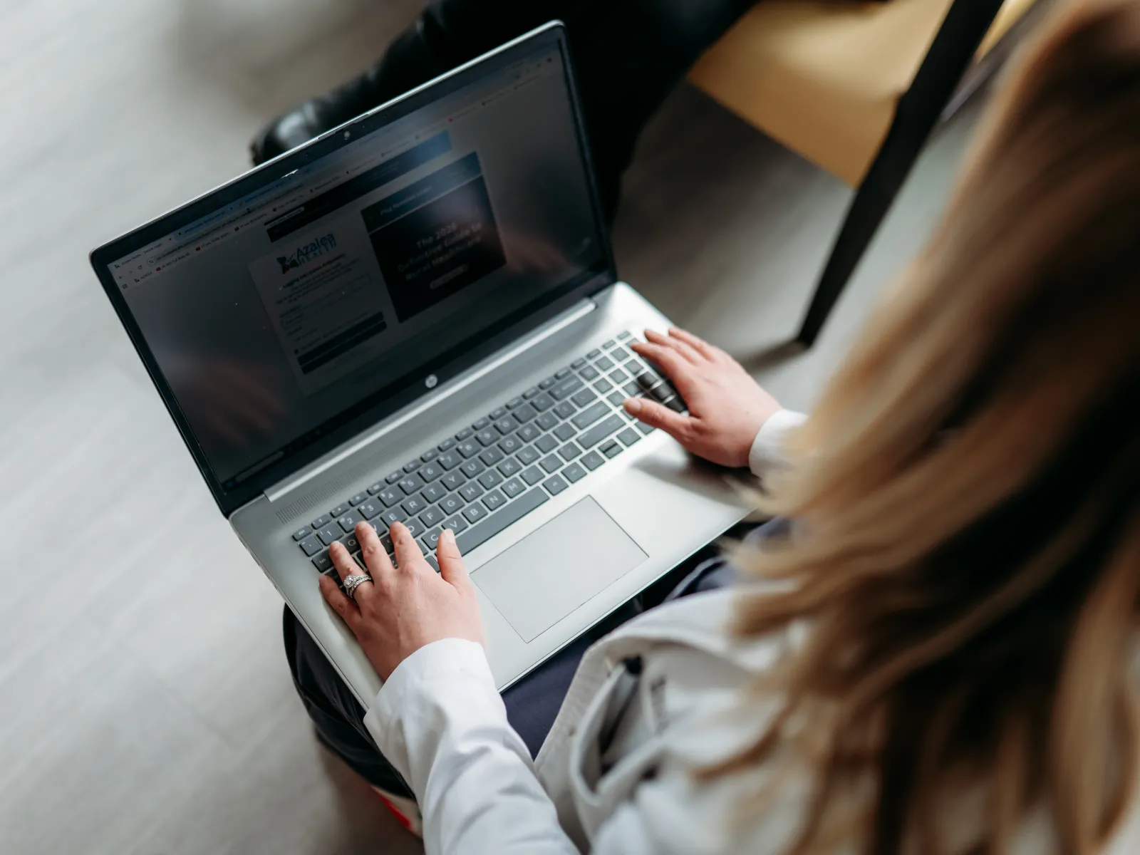 Person using a laptop with both hands typing on the keyboard in a bright indoor space.