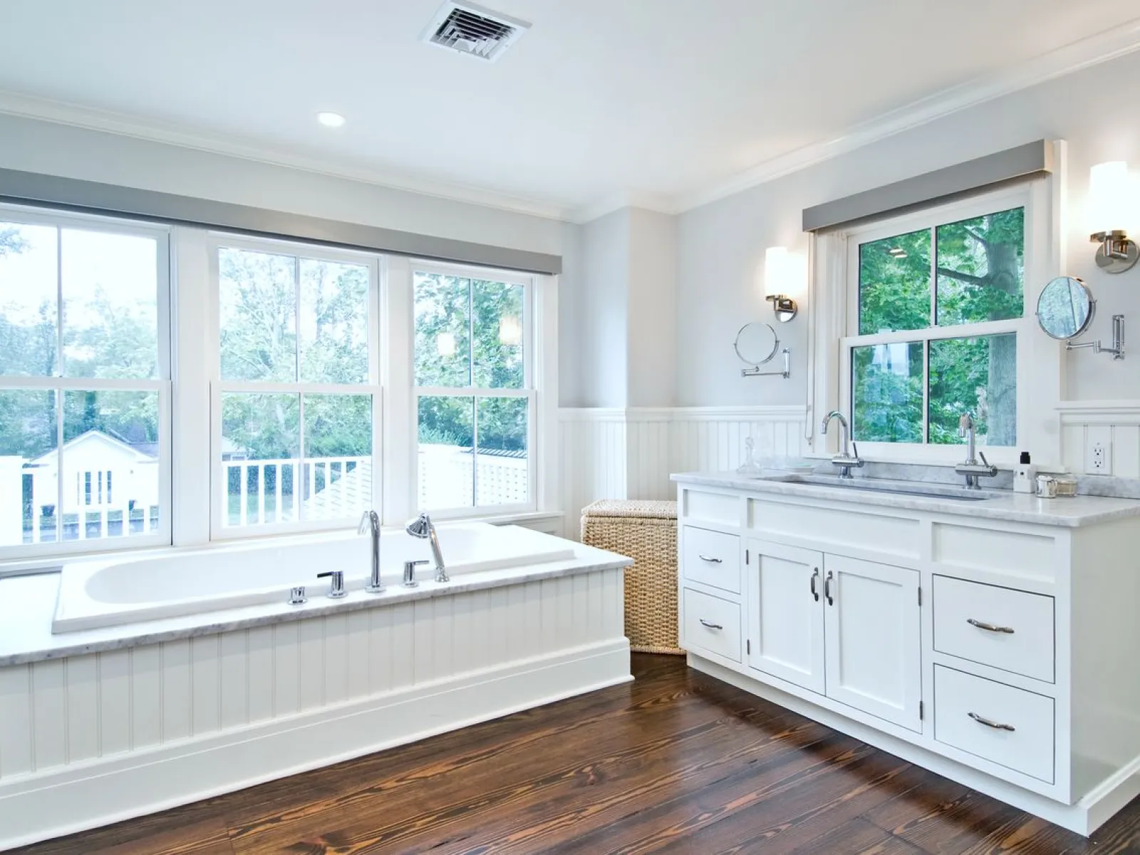 Bright, modern bathroom with a freestanding tub and dual sink vanity featuring large windows and hardwood floors.