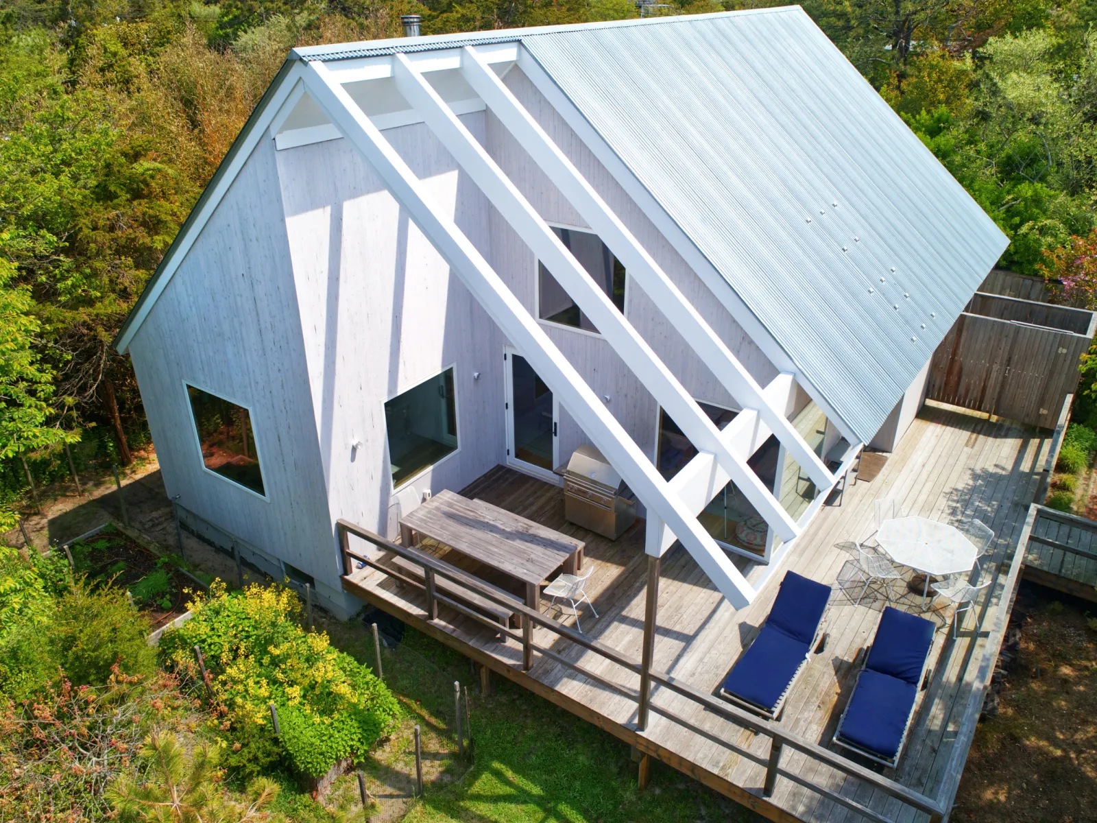Modern wooden house with sloped roof, large windows, and outdoor seating area surrounded by greenery.
