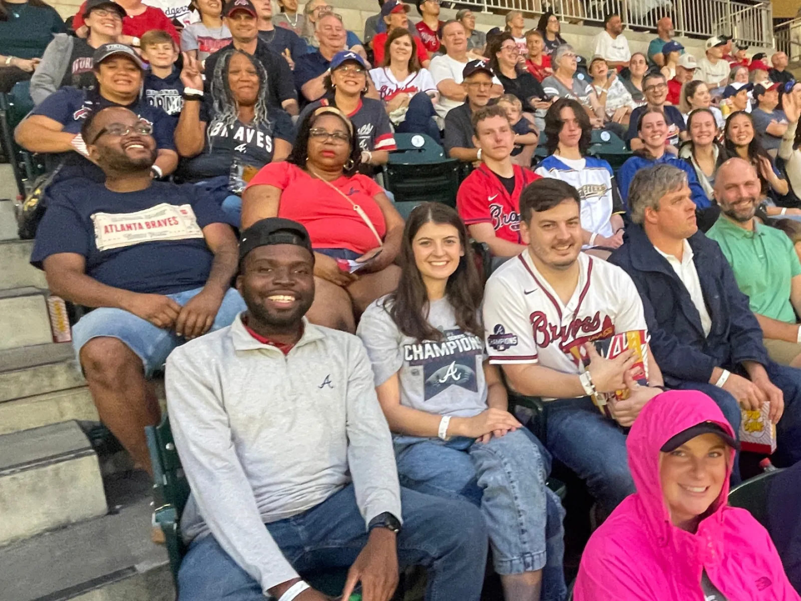 Diverse fans wearing Braves apparel enjoying a baseball game in stadium bleachers on game day.