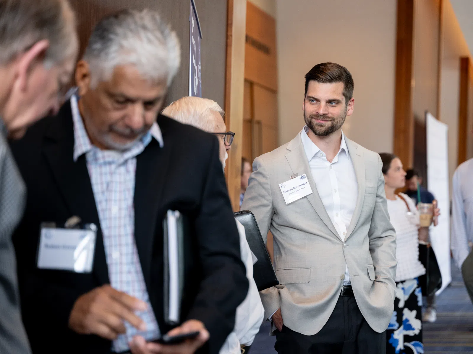 Professional networking event with businessmen and women in formal attire engaging and socializing in a conference hallway.