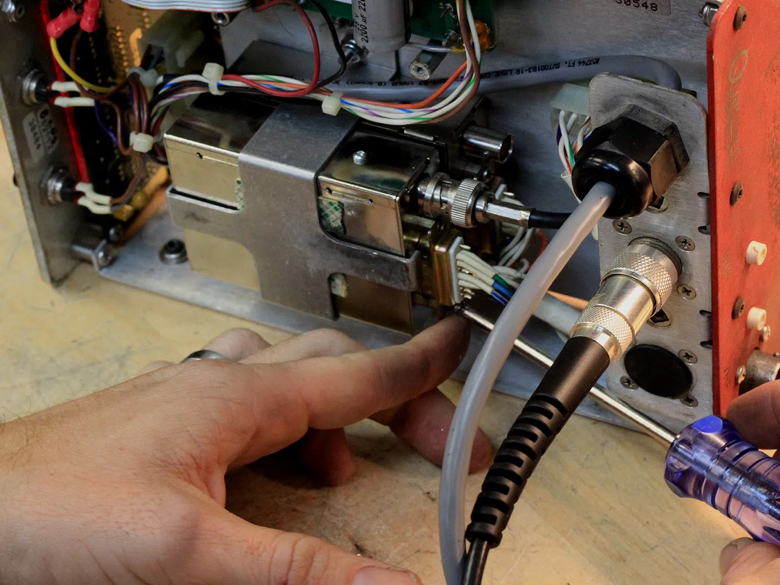 Technician repairing or maintaining complex electronic device with cables and screwdriver on wooden surface