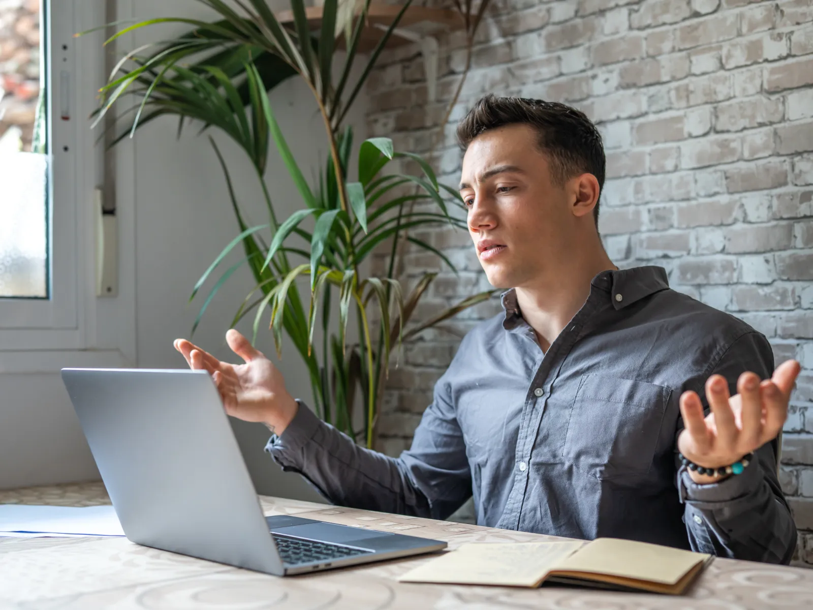 a man sitting at a table with a laptop and a plant