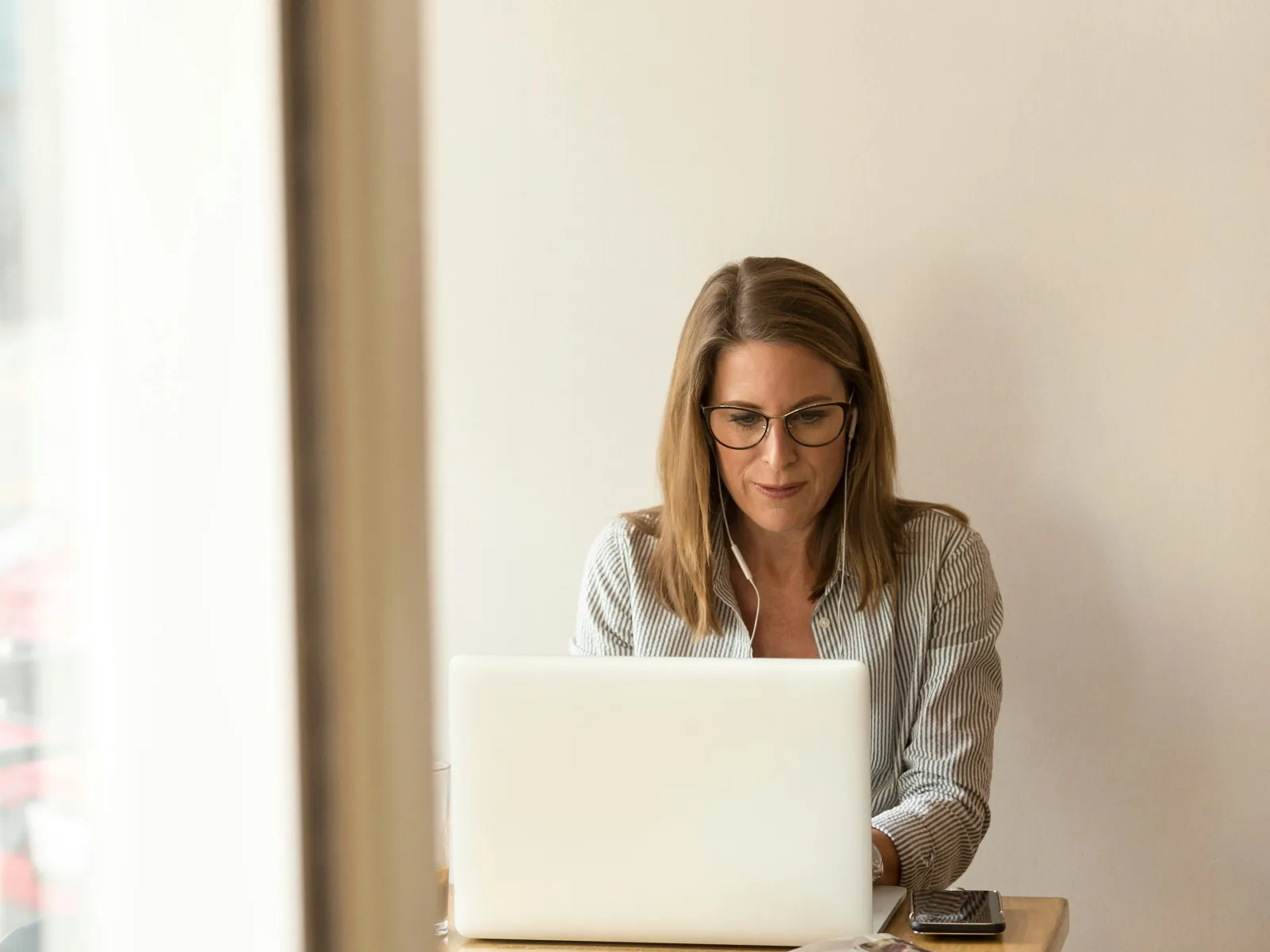 Woman working on a laptop at a wooden table, focused and productive in a bright, minimalistic setting.