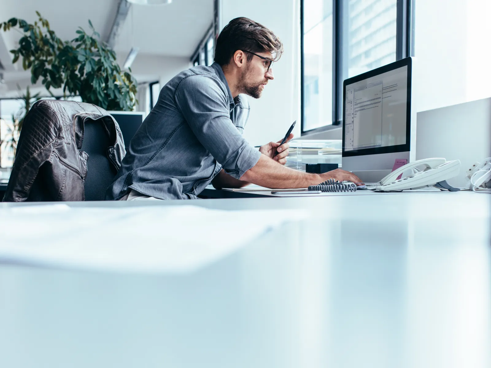 a man sitting at a desk with a computer and a pen