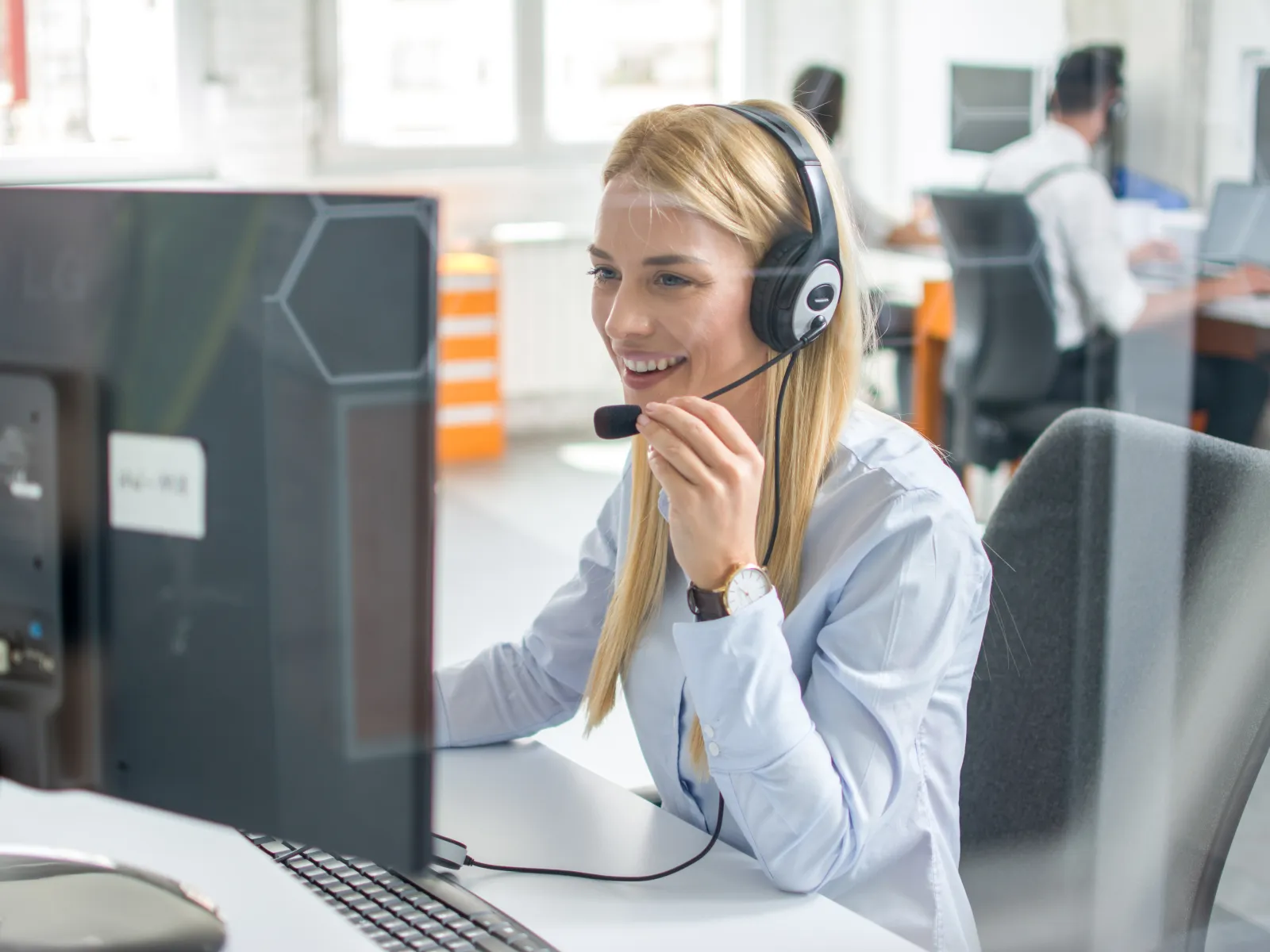 Smiling female customer service representative wearing headset working on computer in office environment