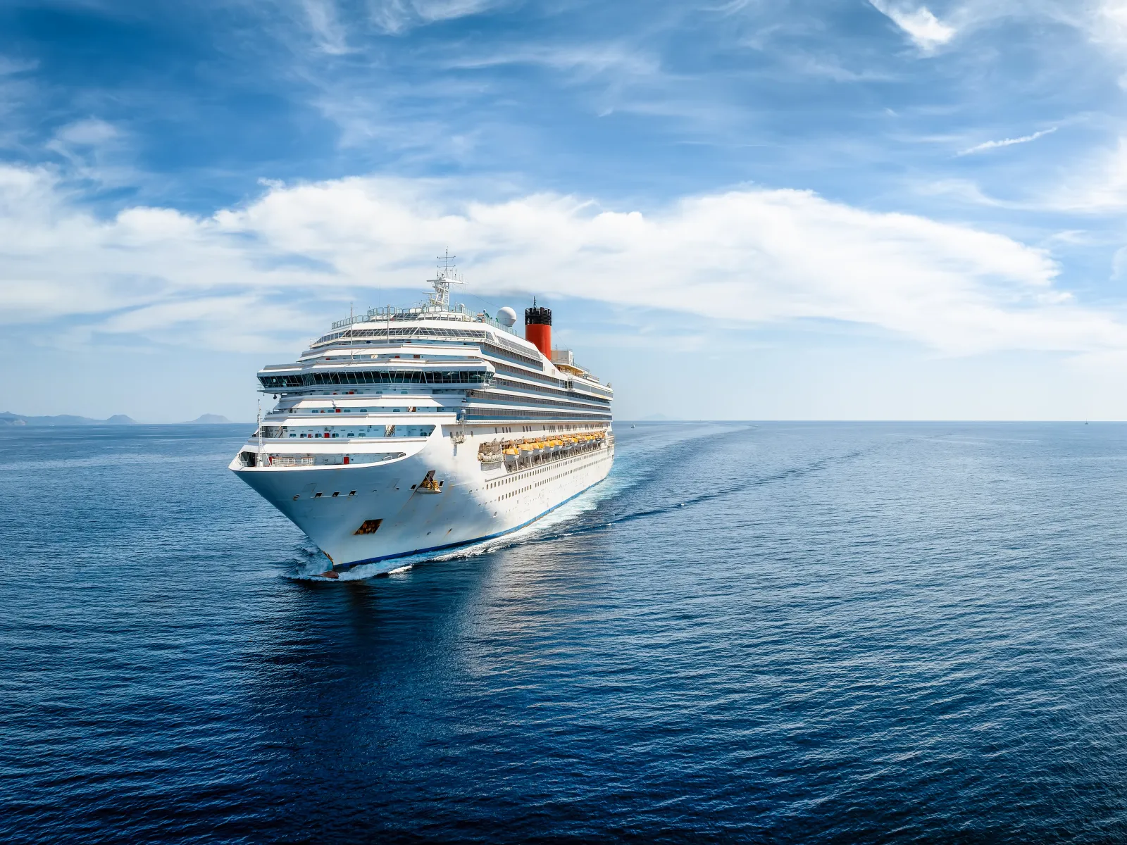 Large white cruise ship sailing on clear blue ocean under a partly cloudy sky during daytime