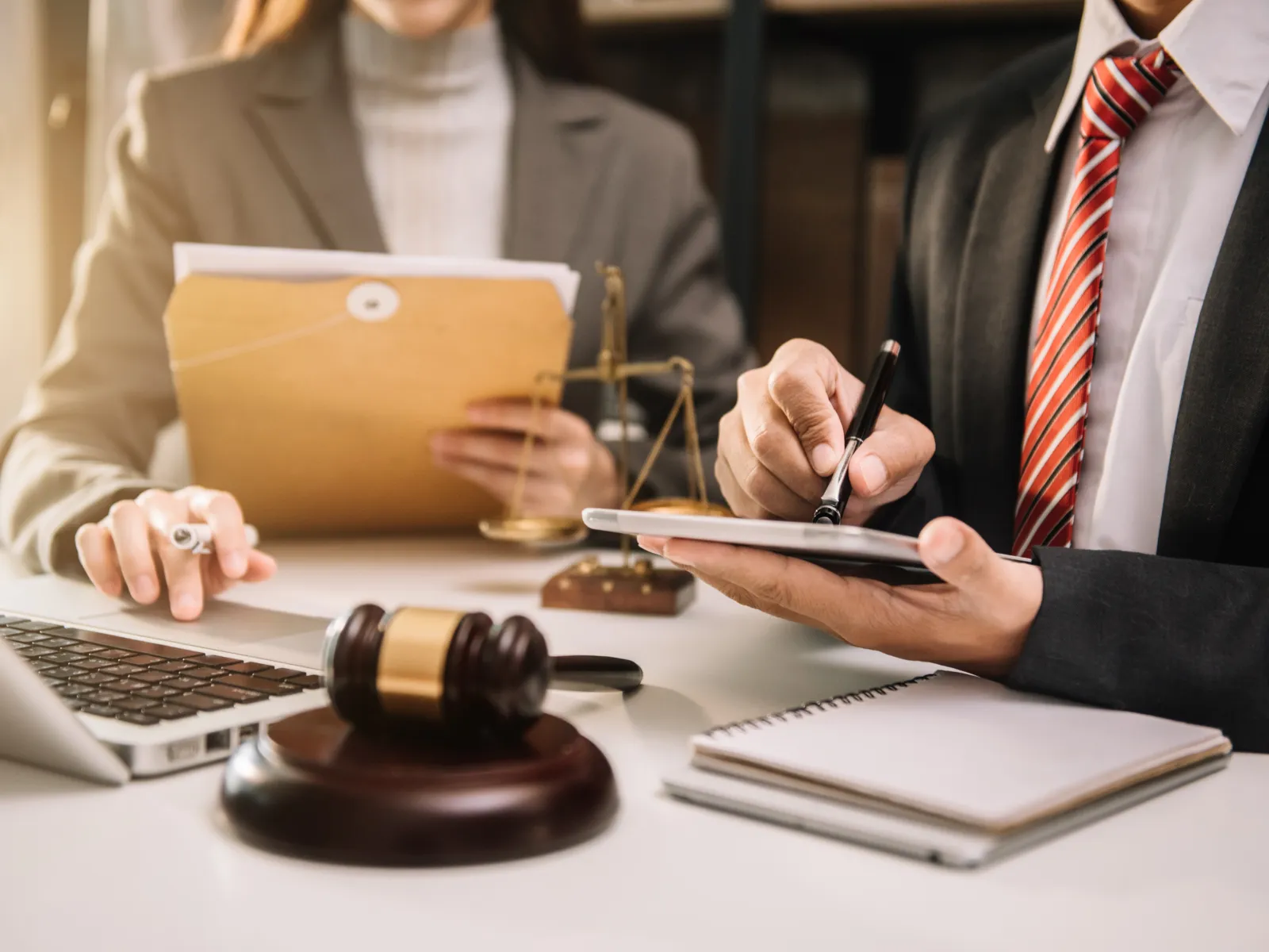 Lawyers in professional attire working with legal documents, gavel, scales, and laptop in office setting.