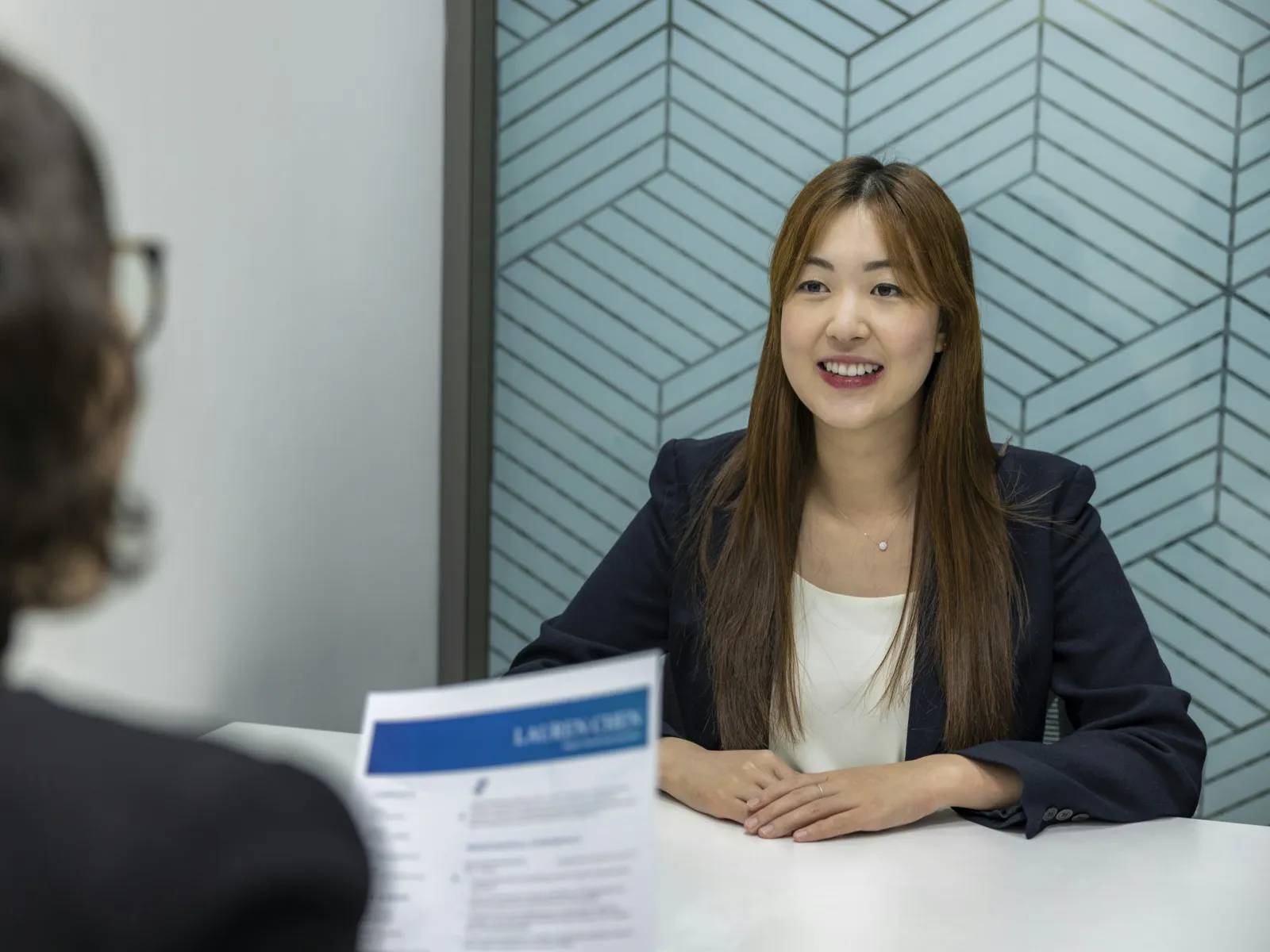 A young woman in business attire smiles during an interview at a modern office.