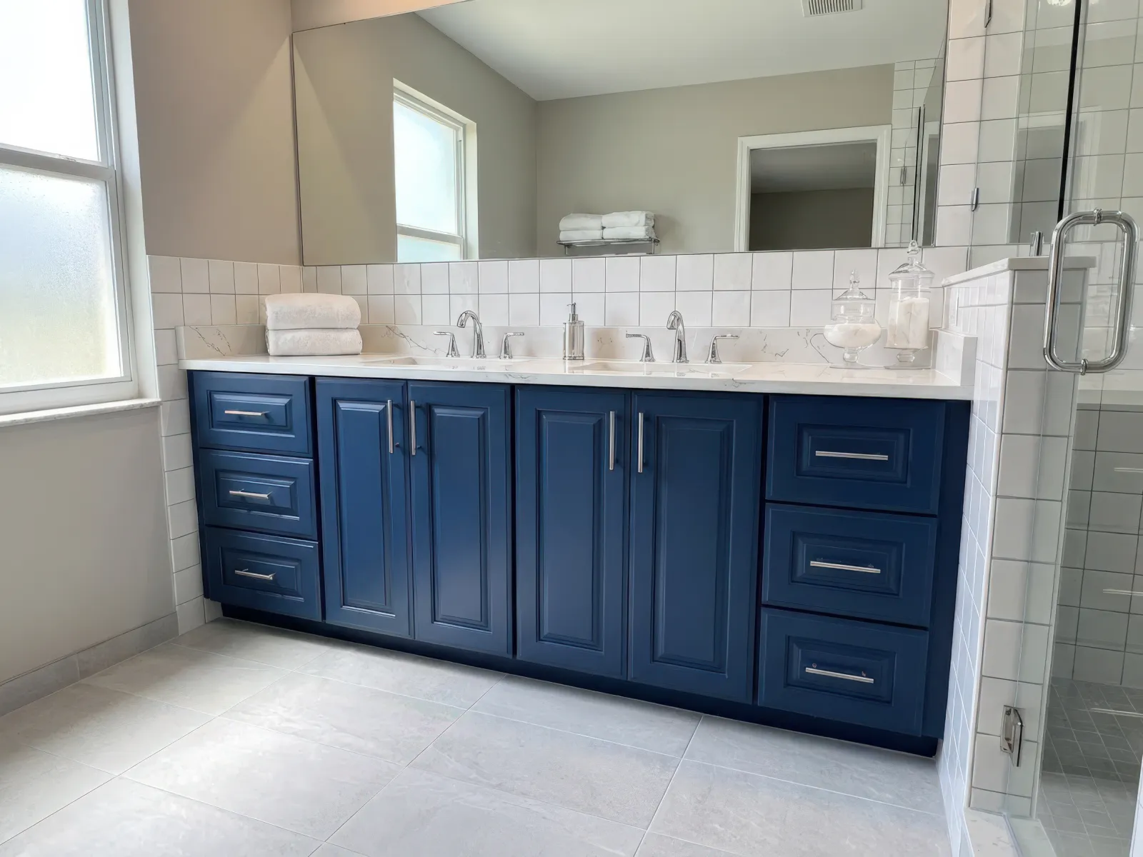 Modern bathroom with navy blue double vanity cabinet, white countertop, dual sinks, and large mirror under natural light.