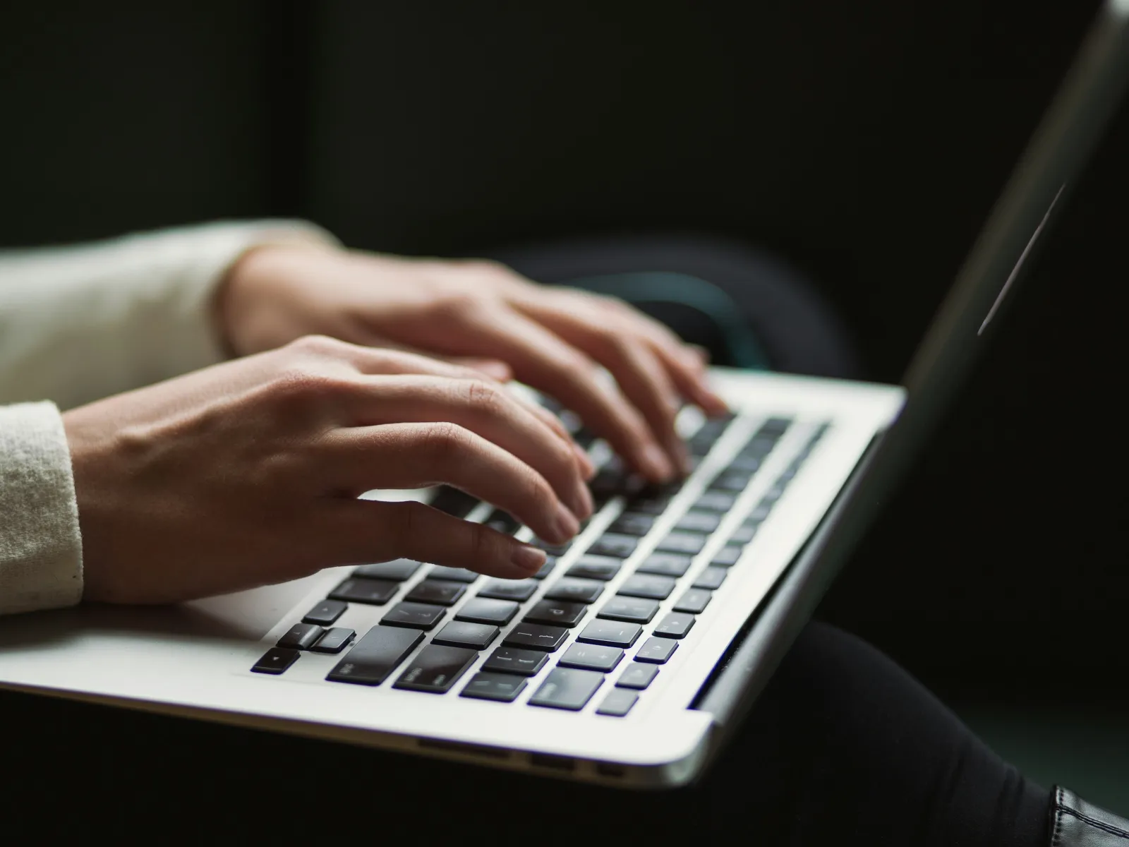 Close-up of hands typing on a laptop keyboard with soft natural lighting and dark background.