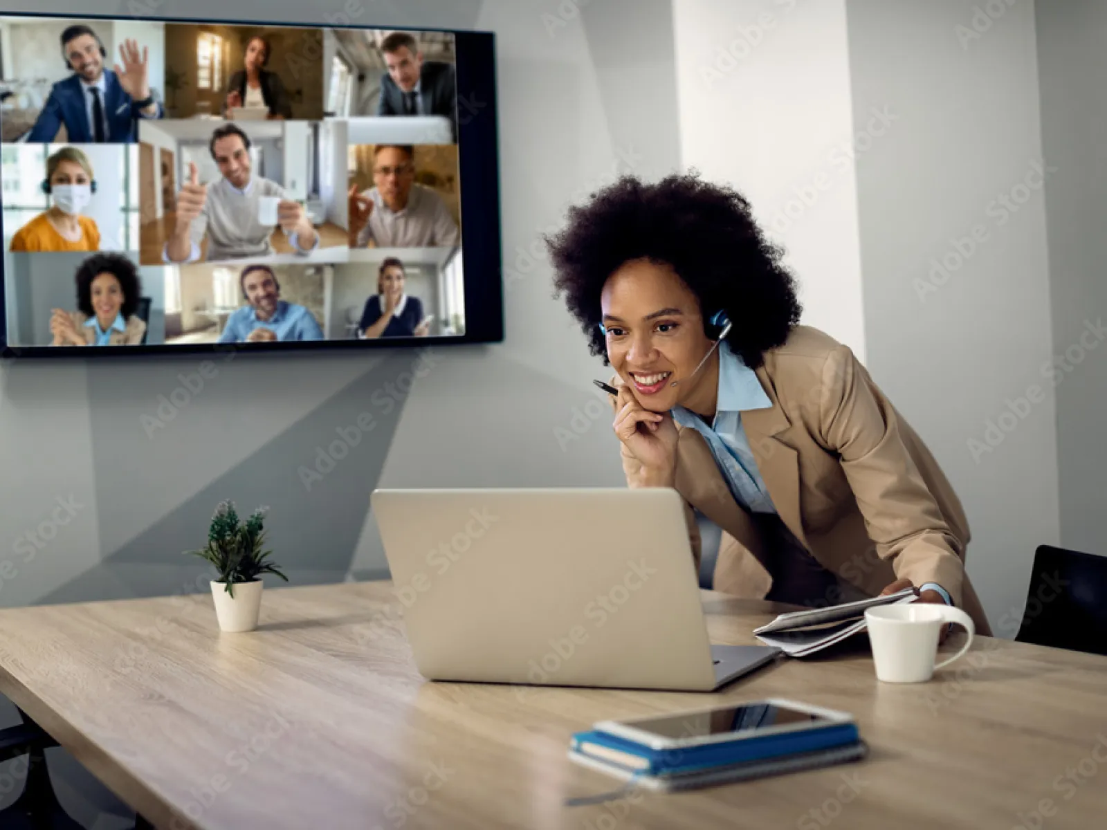 Professional woman on a video call, engaging with diverse attendees in a modern office setting.