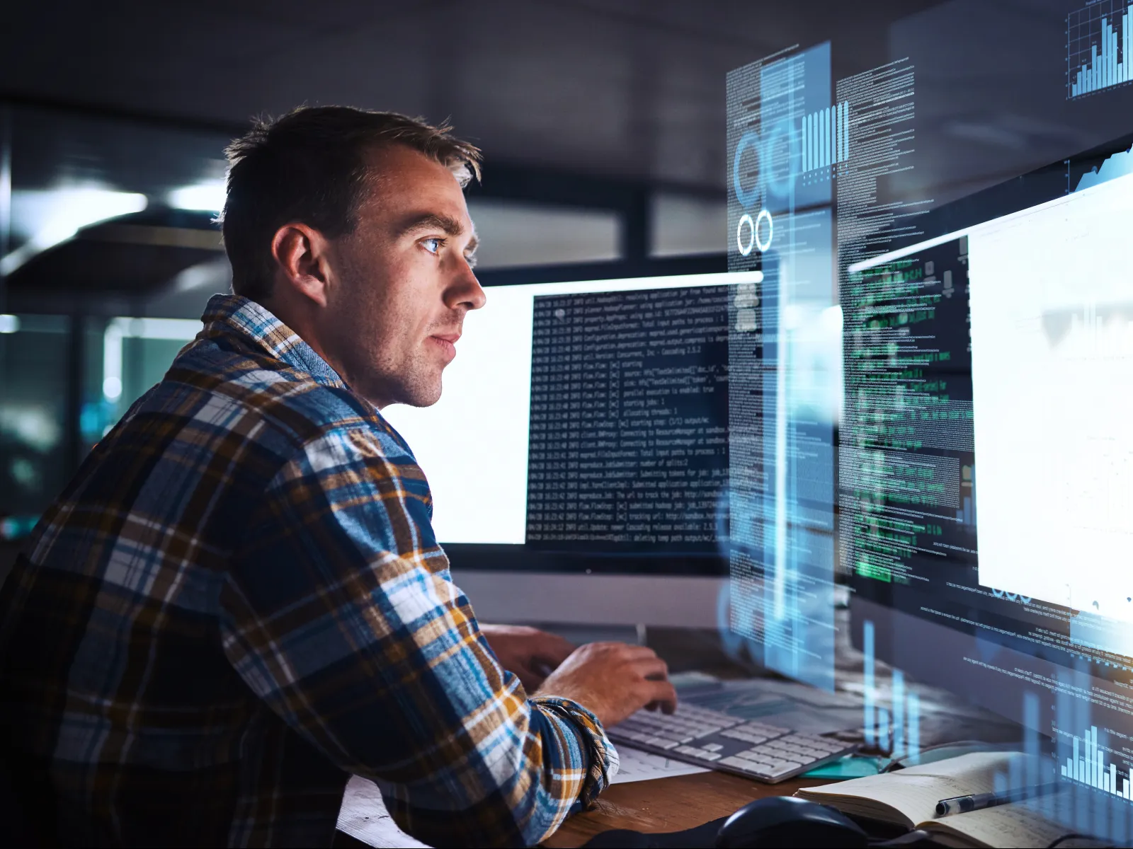 A male programmer working intently on dual monitors filled with code and digital data visualizations.