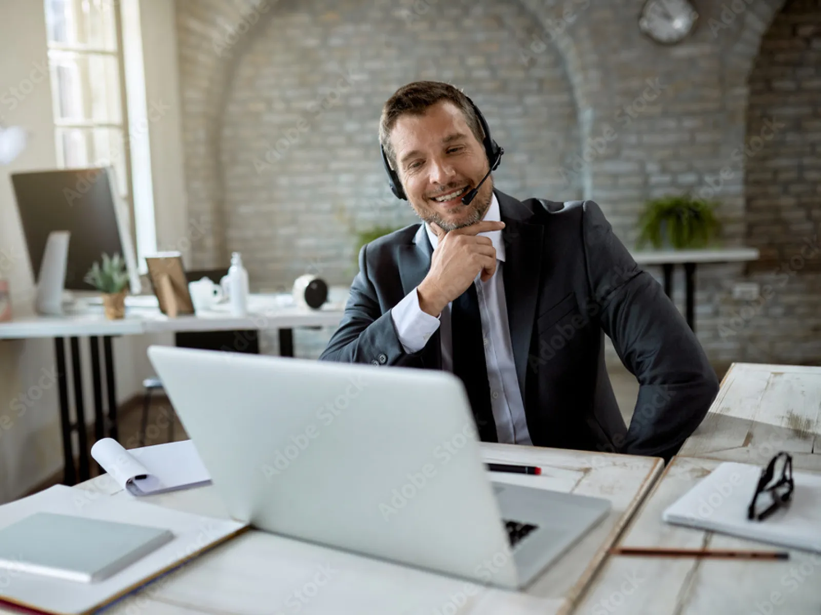 Smiling man in a headset working at a laptop in a modern office environment.