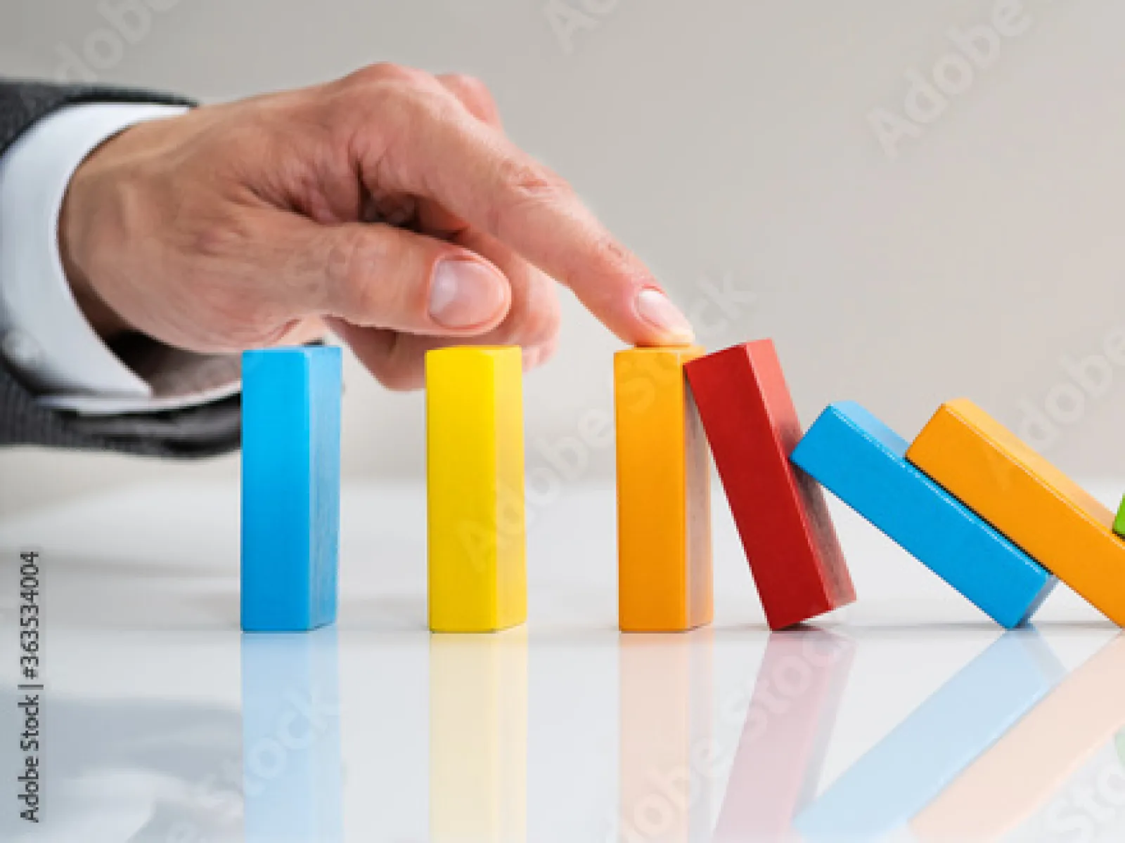 A hand tips colorful dominoes, demonstrating cause and effect dynamics in playful arrangement.
