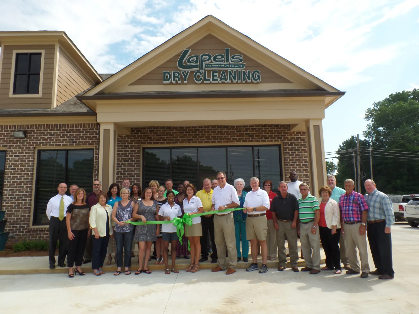 Group of people holding a green ribbon in front of Lapels Dry Cleaning store during a ribbon-cutting event