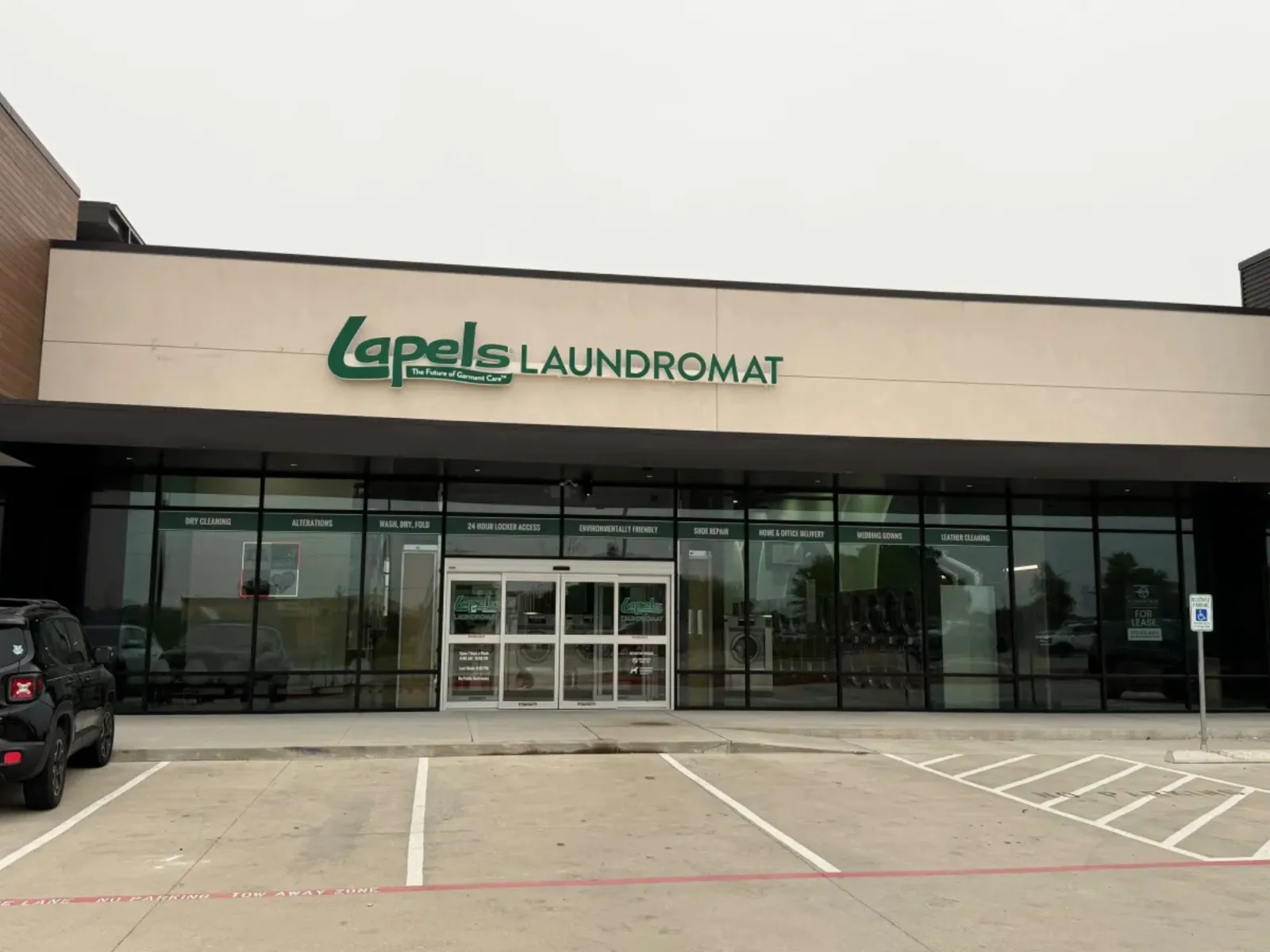 Exterior view of Lapels Laundromat storefront with parking spaces and a black SUV in front