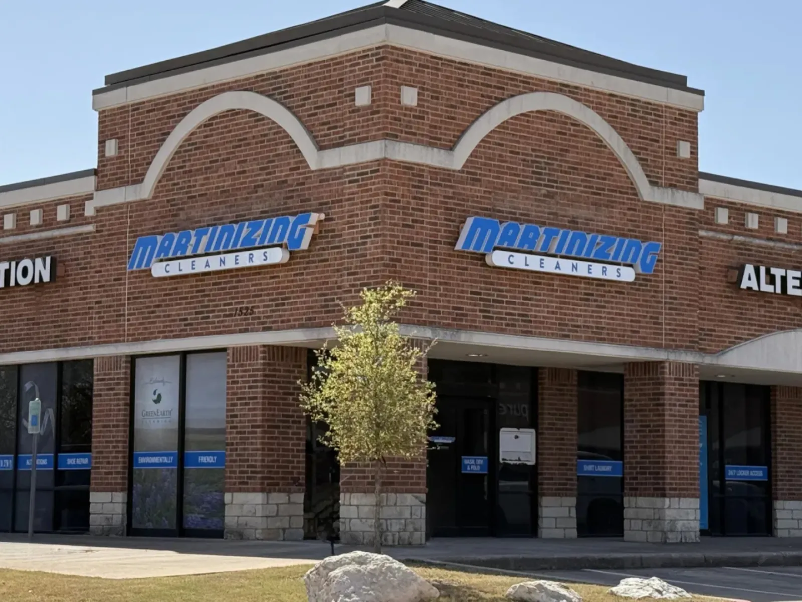 Brick corner building housing Martinizing Cleaners and Alteration services under a clear blue sky.