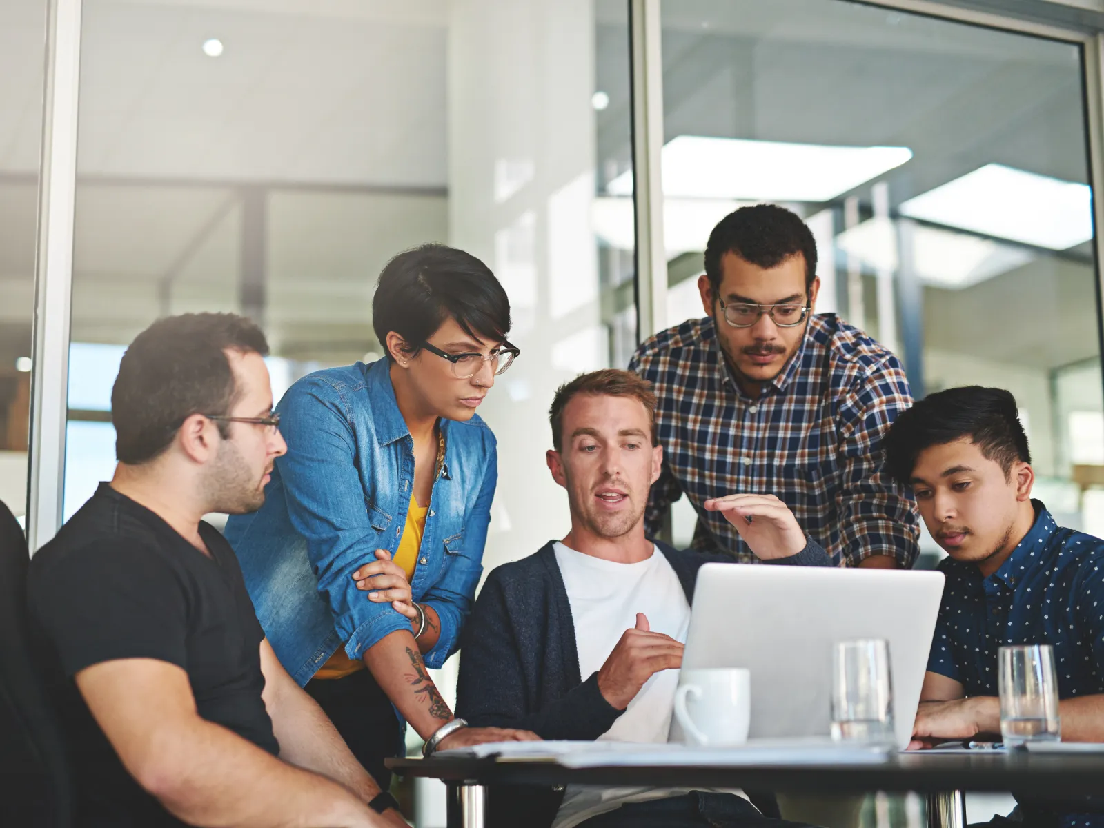 A diverse group of professionals collaborating around a laptop in a modern office setting.