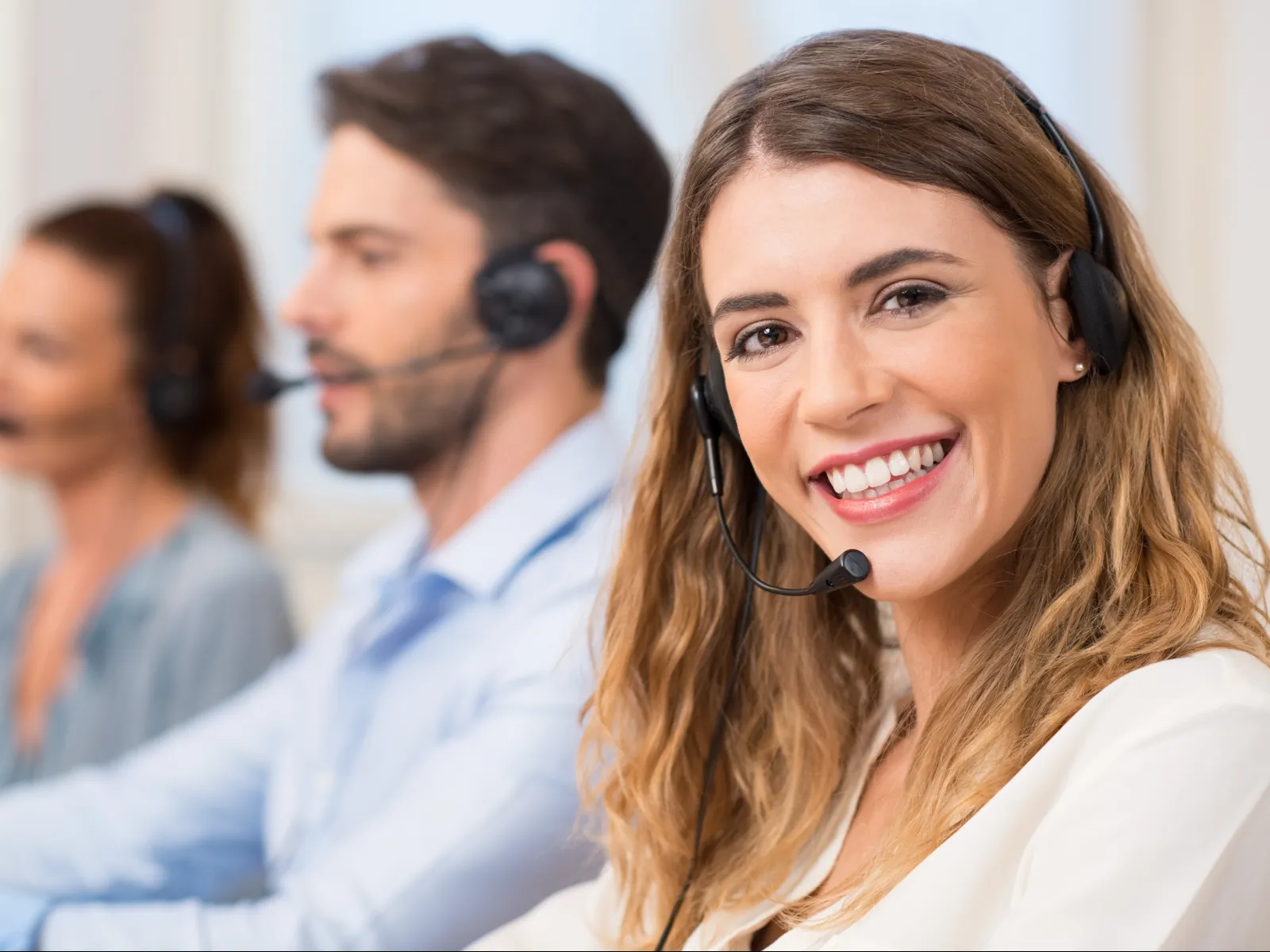 Smiling female call center agent wearing headset with colleagues working in background in office environment