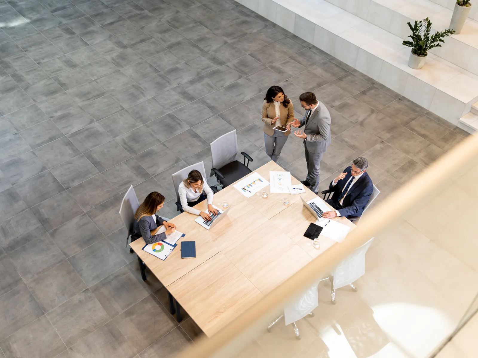 Overhead view of business team collaborating around a large wooden table in a modern office lobby.