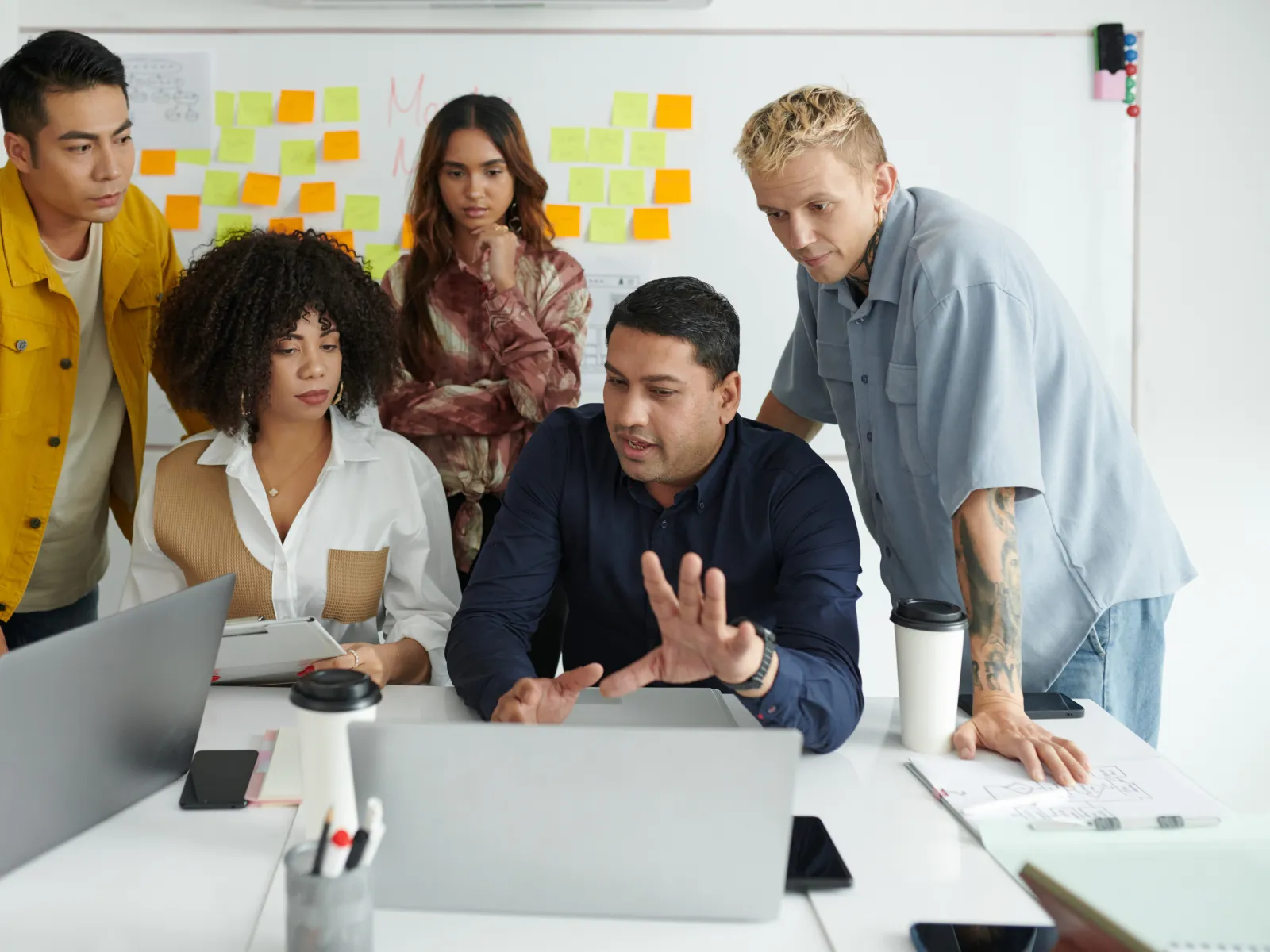 Diverse group of professionals collaborating and discussing work around a laptop in modern office space