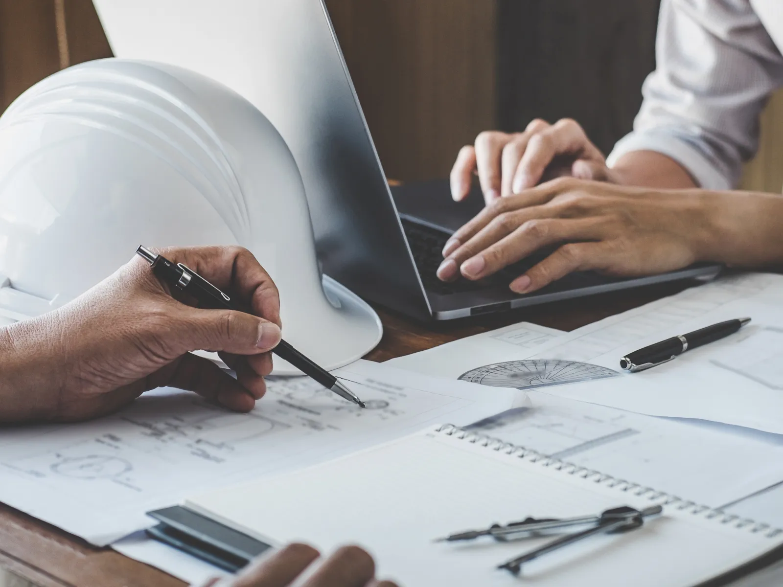 Architects discussing blueprints with a hard hat and drafting tools on the table during planning.