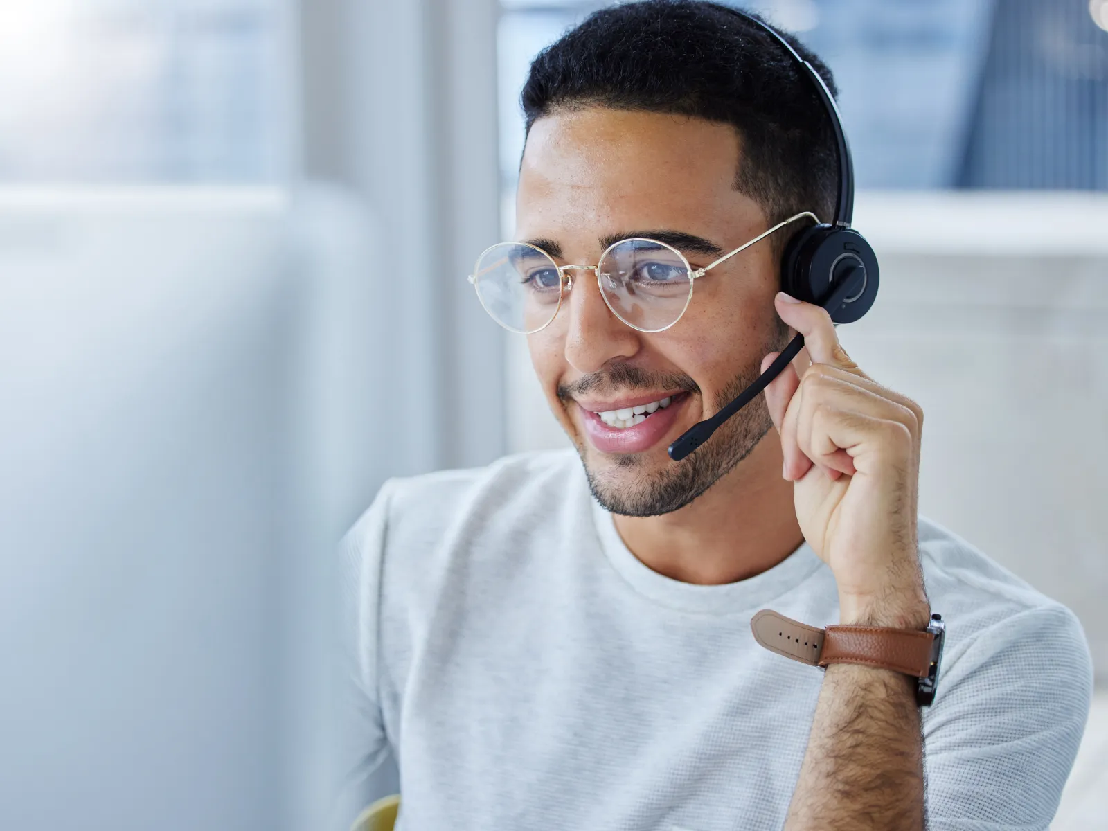 Smiling man wearing glasses and headset, engaged in a video call at his desk.