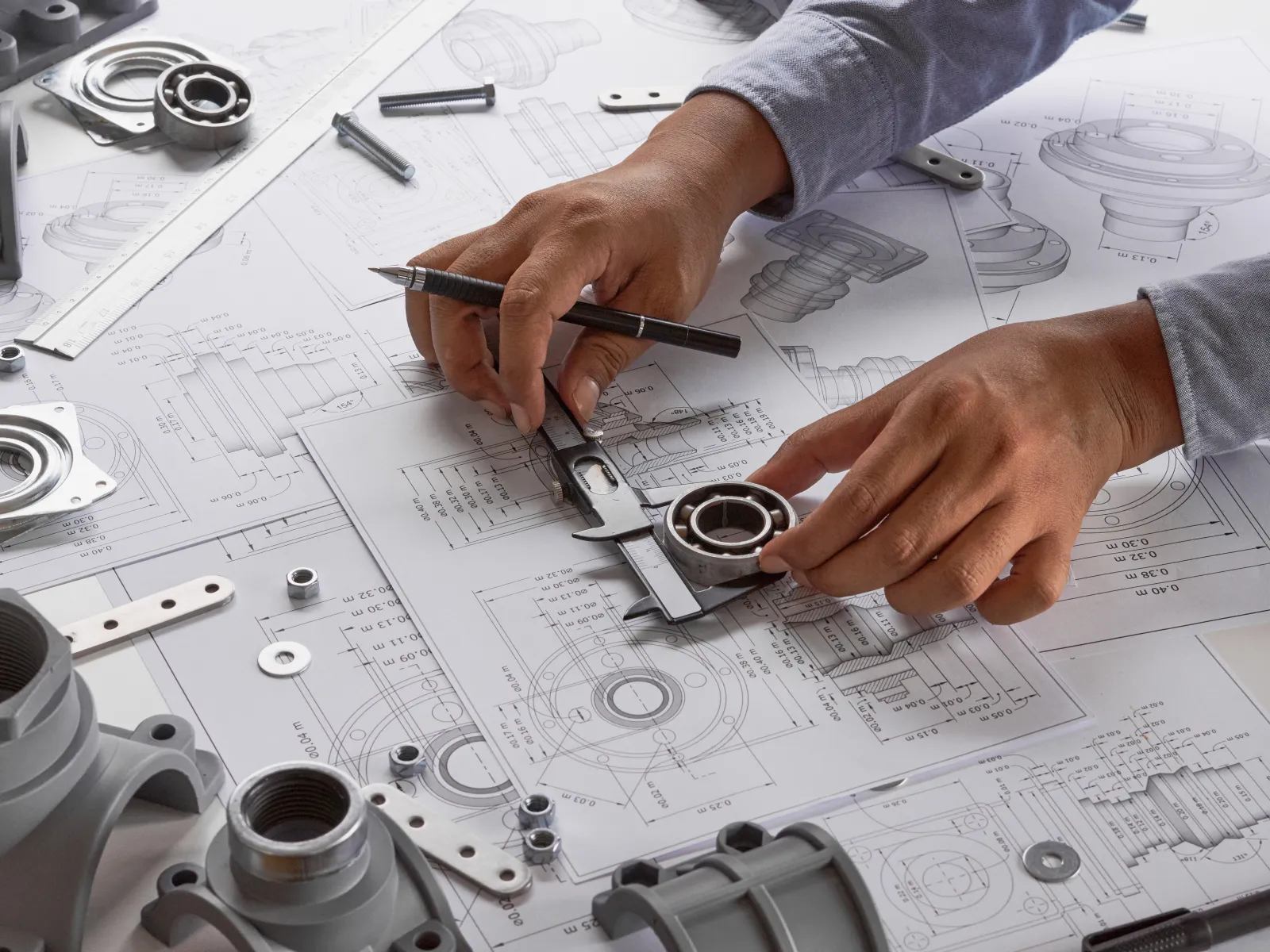 Engineer measuring a bearing with a caliper on technical mechanical blueprint drawings.