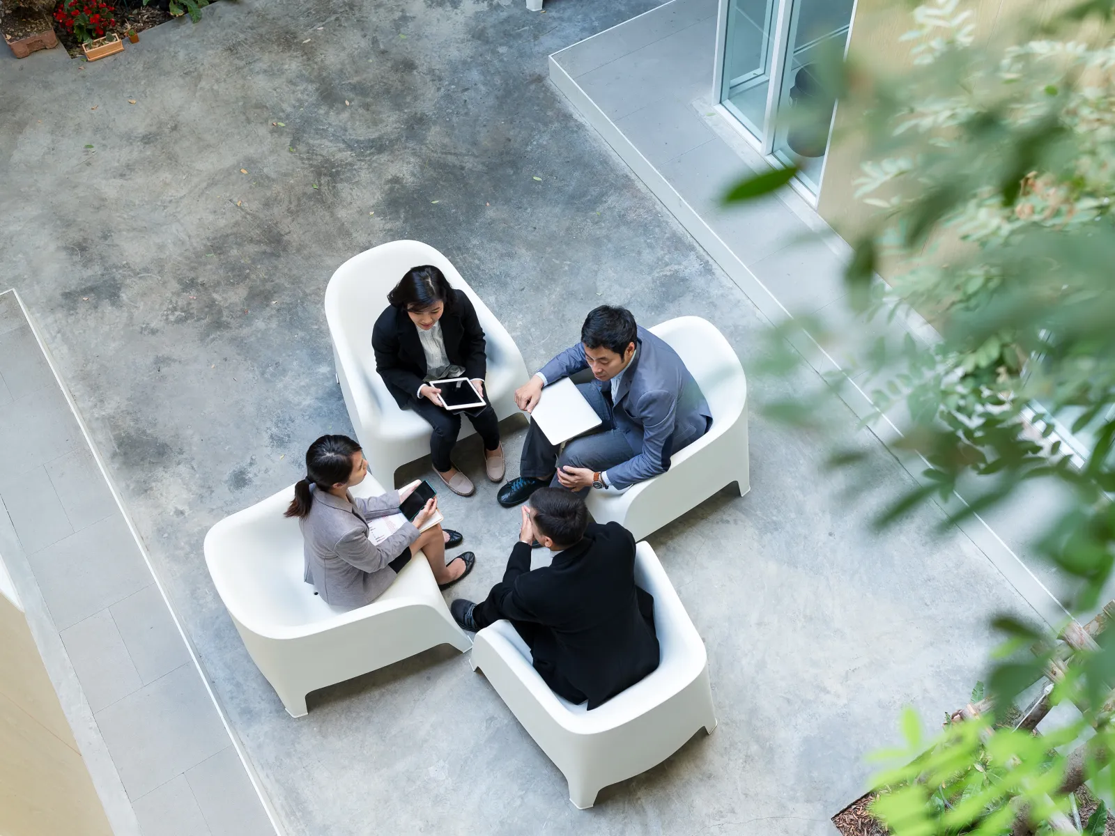 Overhead view of four business professionals in white chairs having a discussion in an open modern office space.