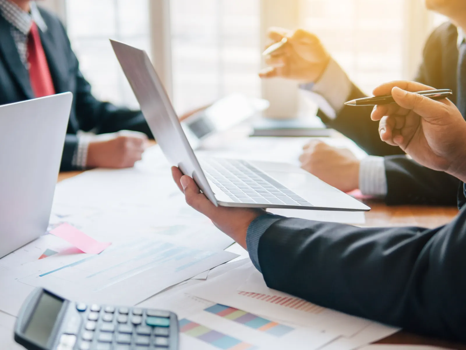 Business professionals in suits discussing financial charts with laptop and calculator on table