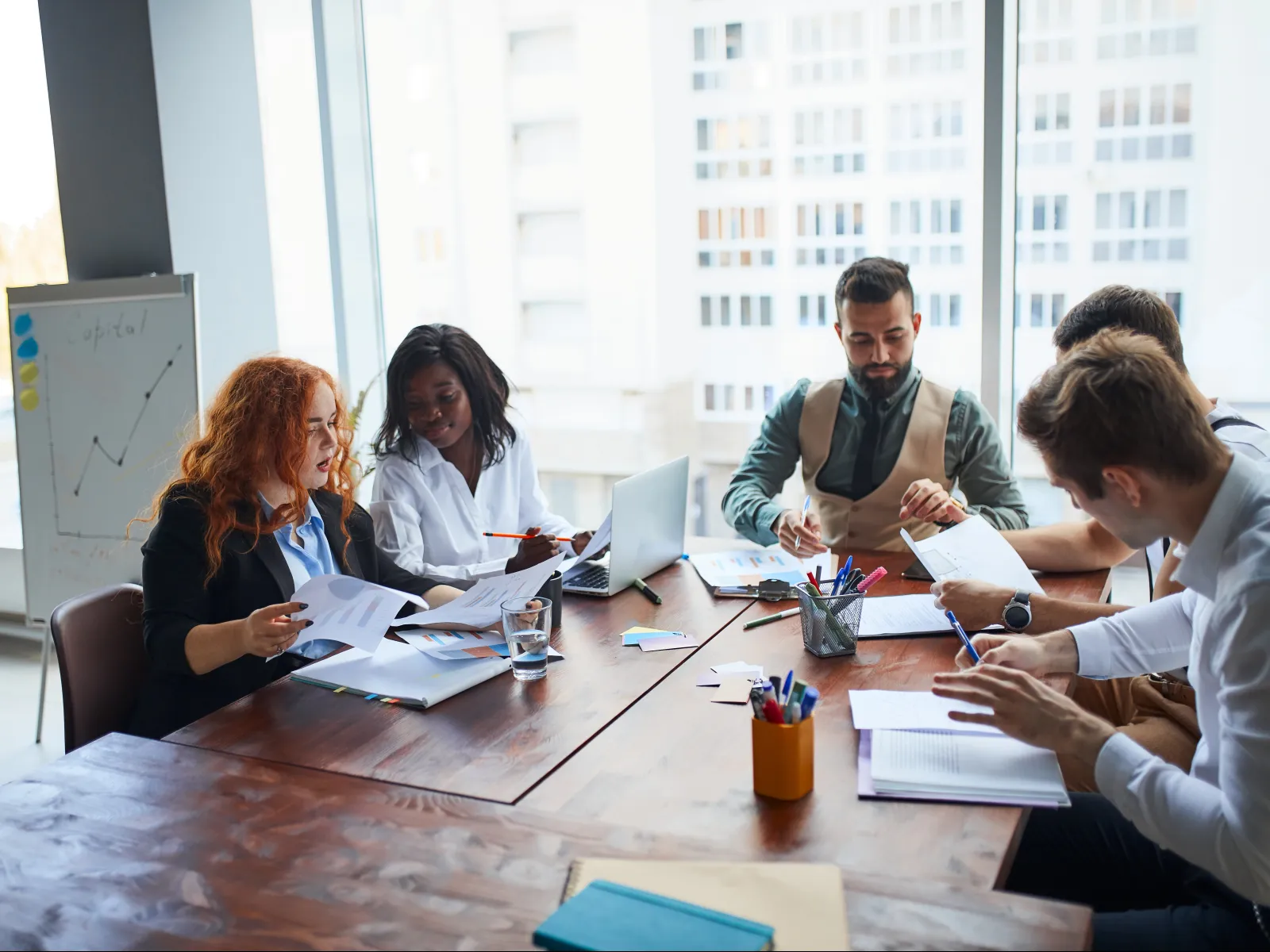 Diverse team collaborating and reviewing documents around a conference table in a modern office space.