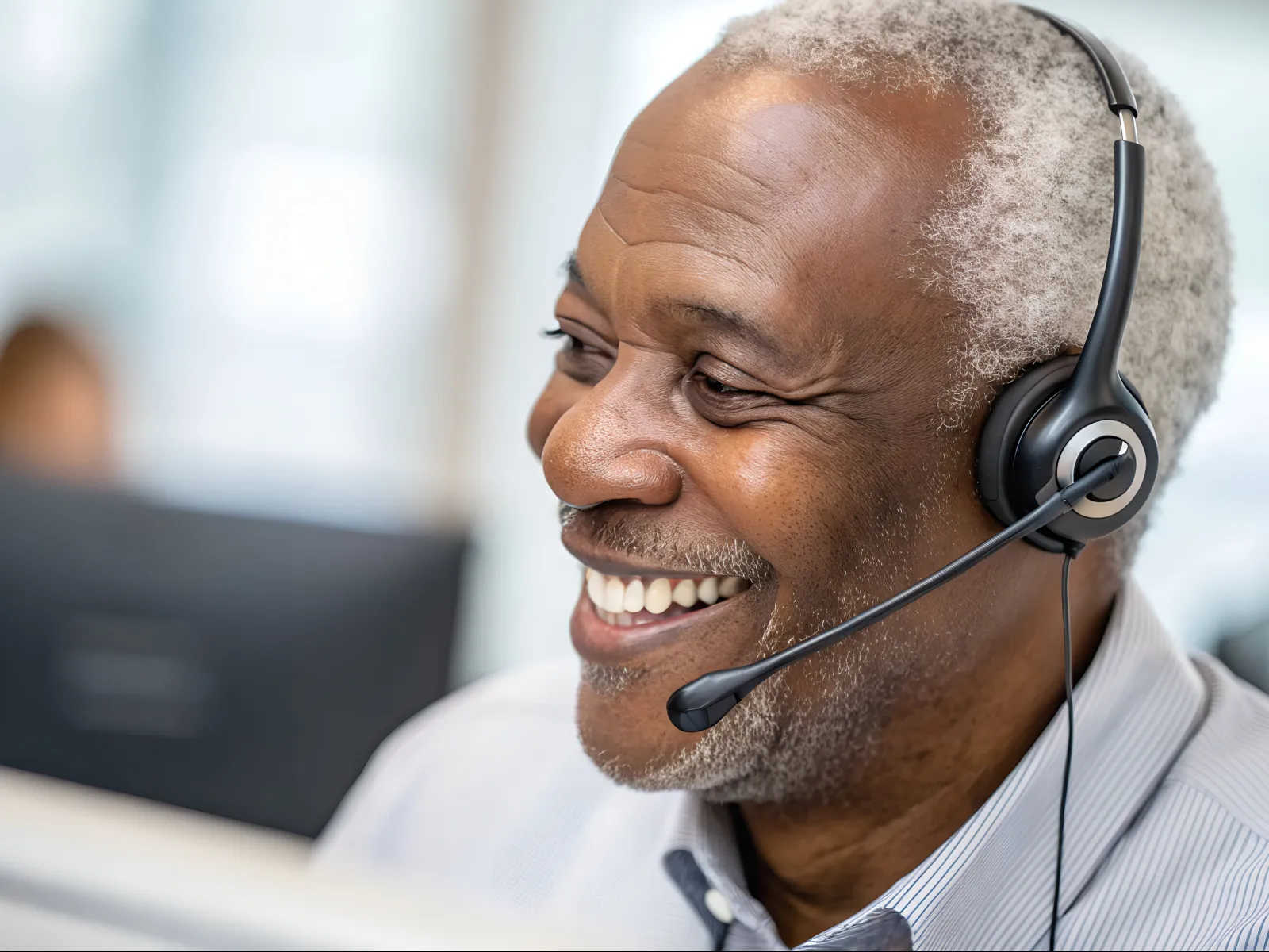 Smiling mature man wearing headset at work, providing customer support in bright office environment