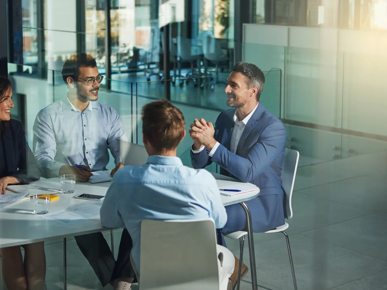 Four professionals engaged in a business meeting around a white table with documents in a modern office.
