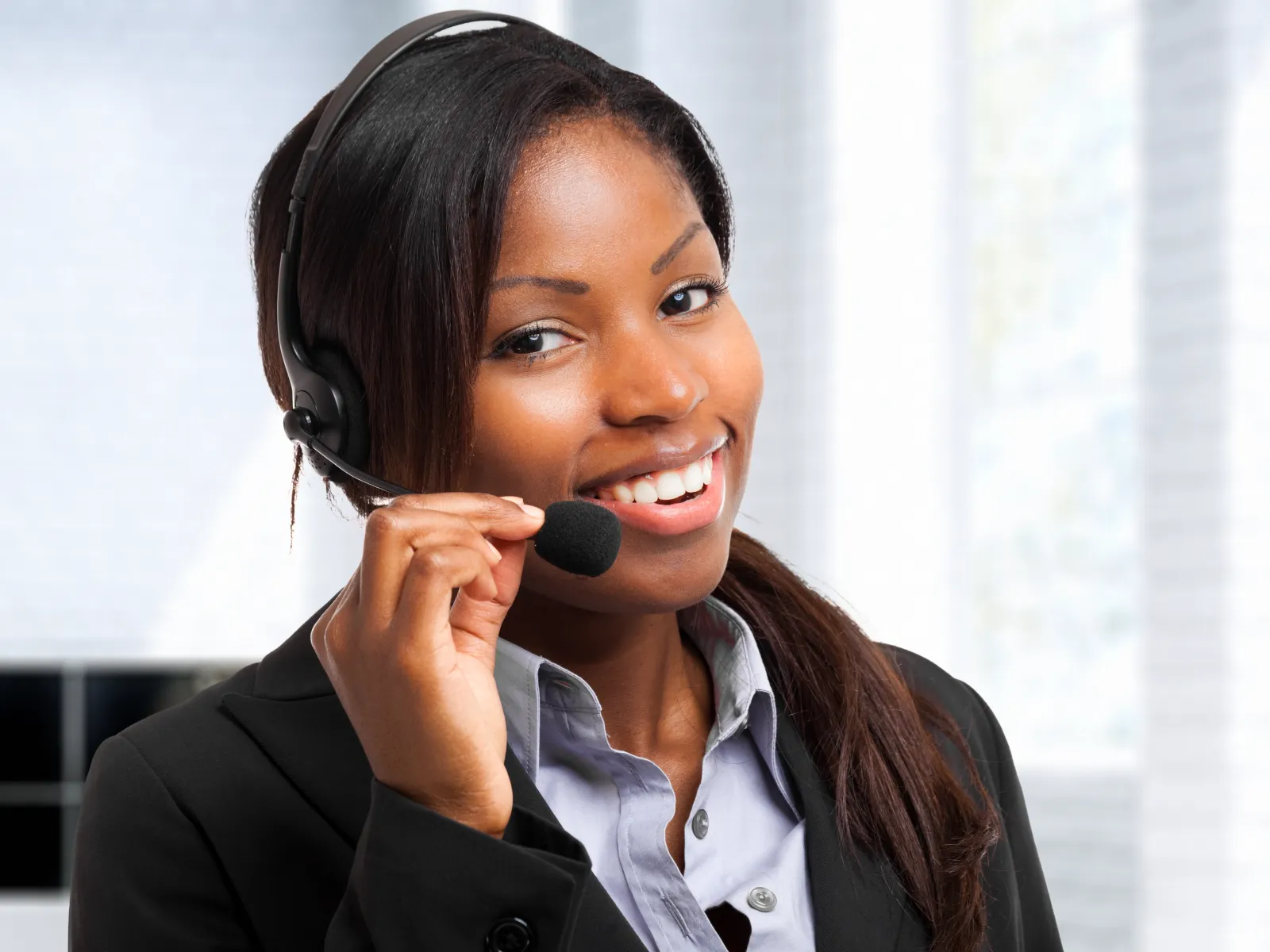 Smiling customer service representative wearing a headset and black blazer in bright office setting