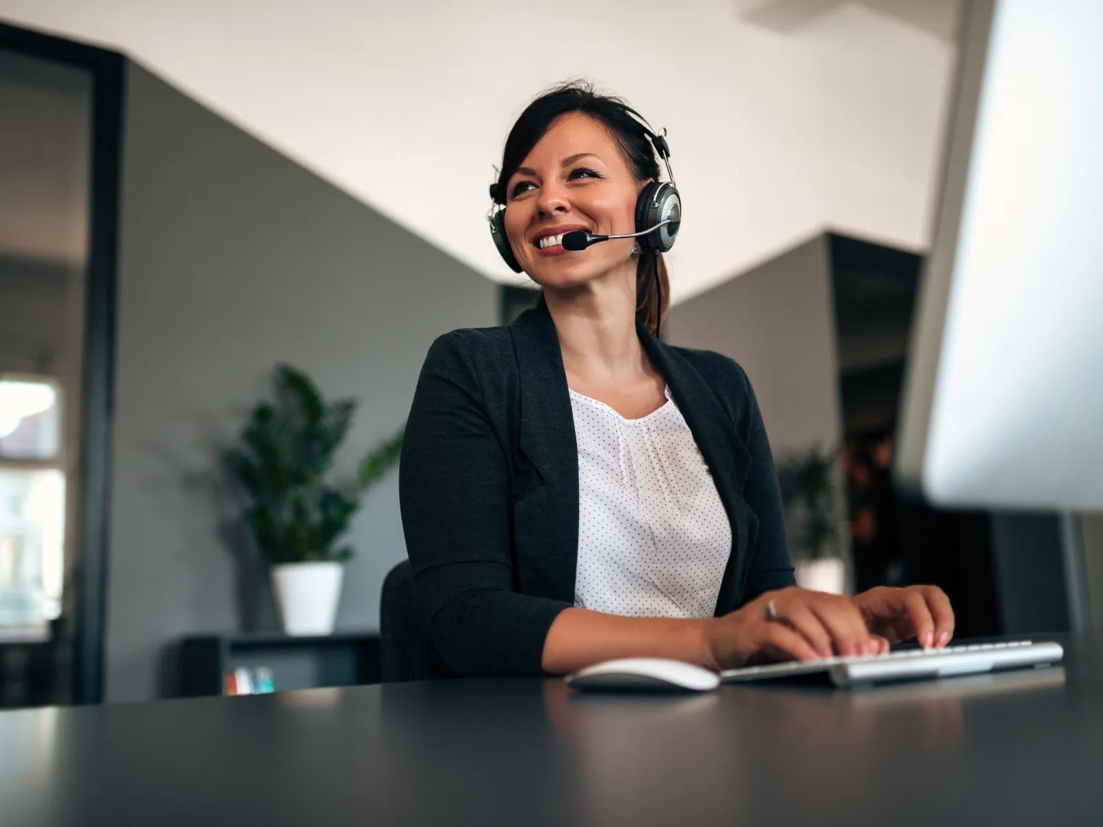 Smiling customer service representative wearing headset typing on keyboard in modern office environment