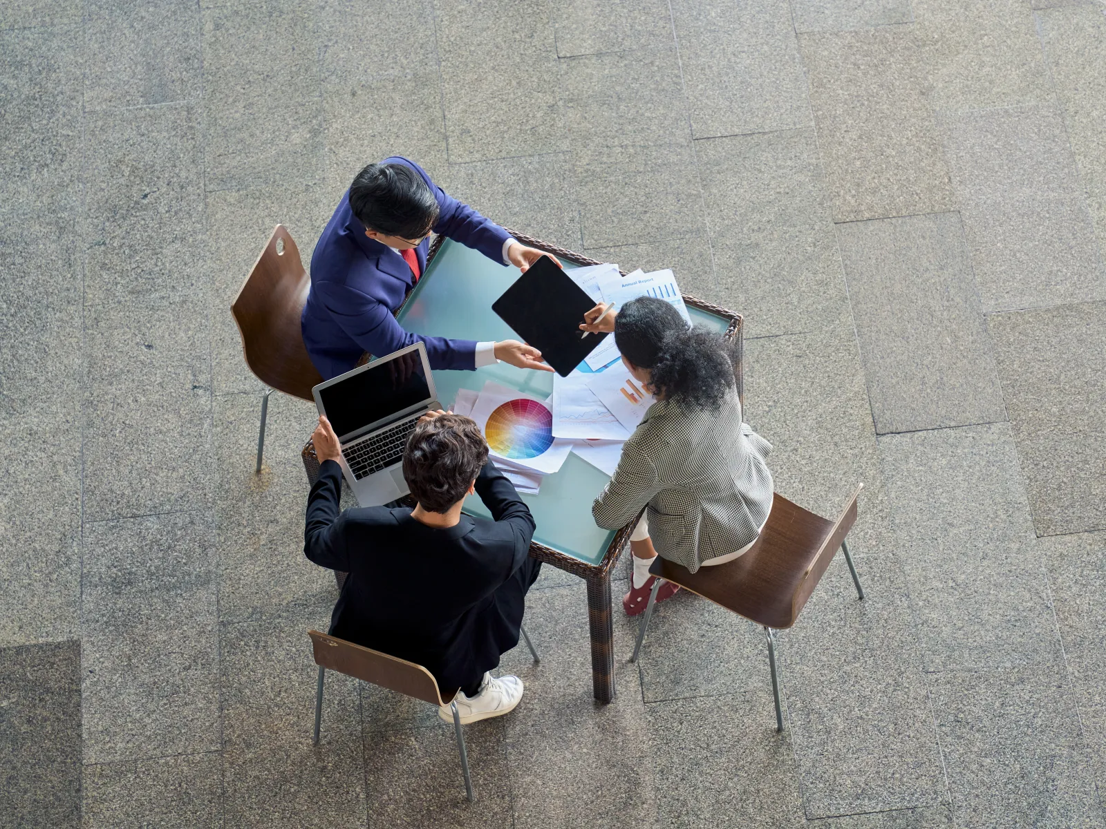 Top view of three people collaborating at a table with laptops, documents, and color wheel charts.