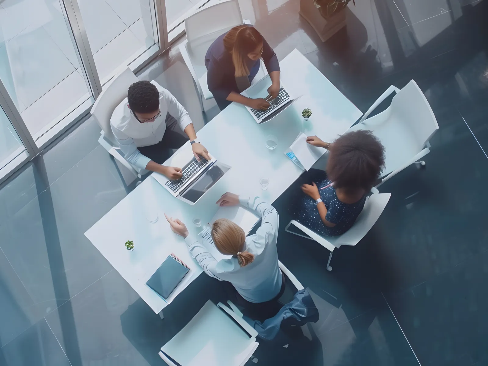 Overhead view of diverse business team collaborating around a white table with laptops in a modern office.